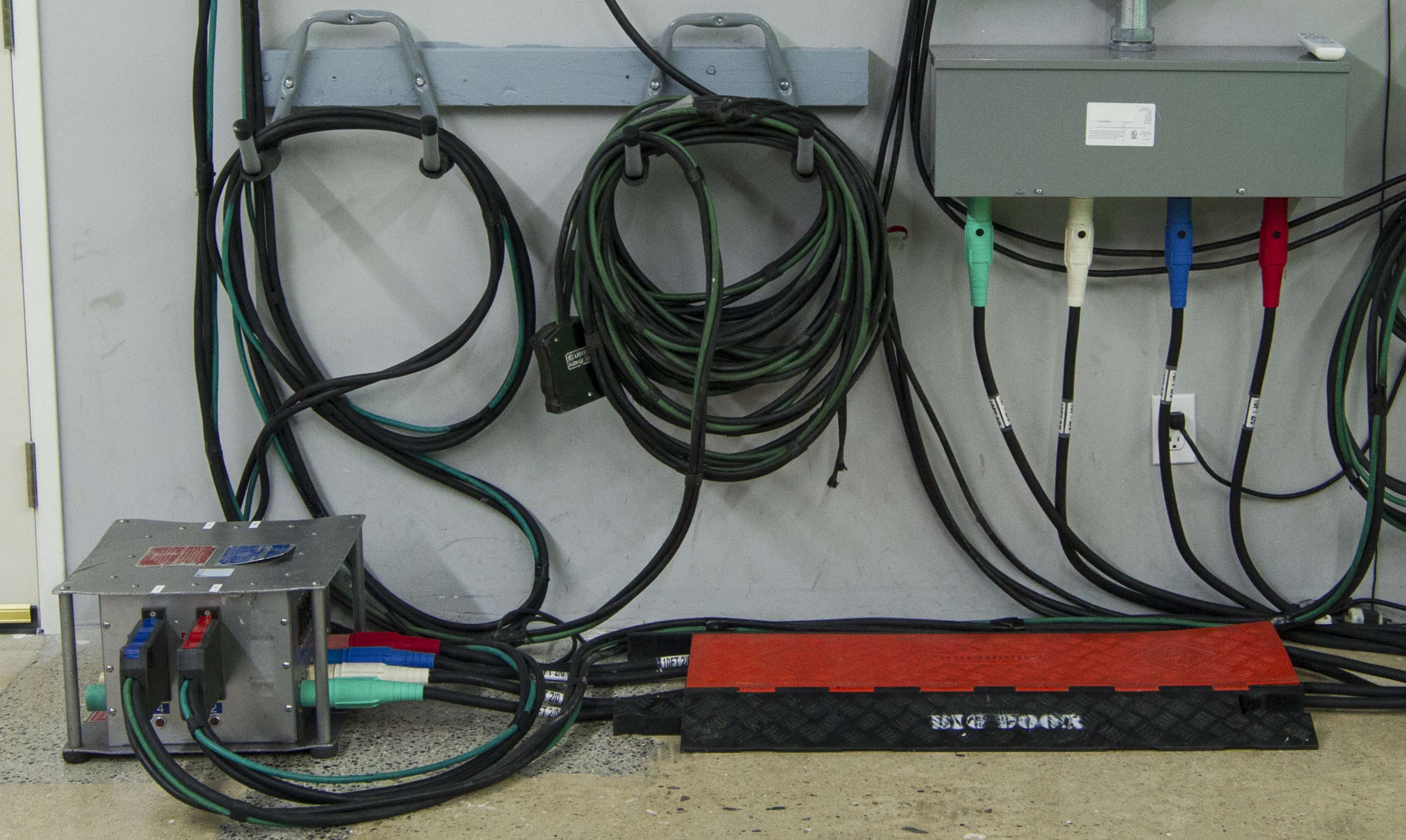 A set of electrical cables and connections neatly organized along a wall, with a junction box mounted above and a cable protector on the floor.