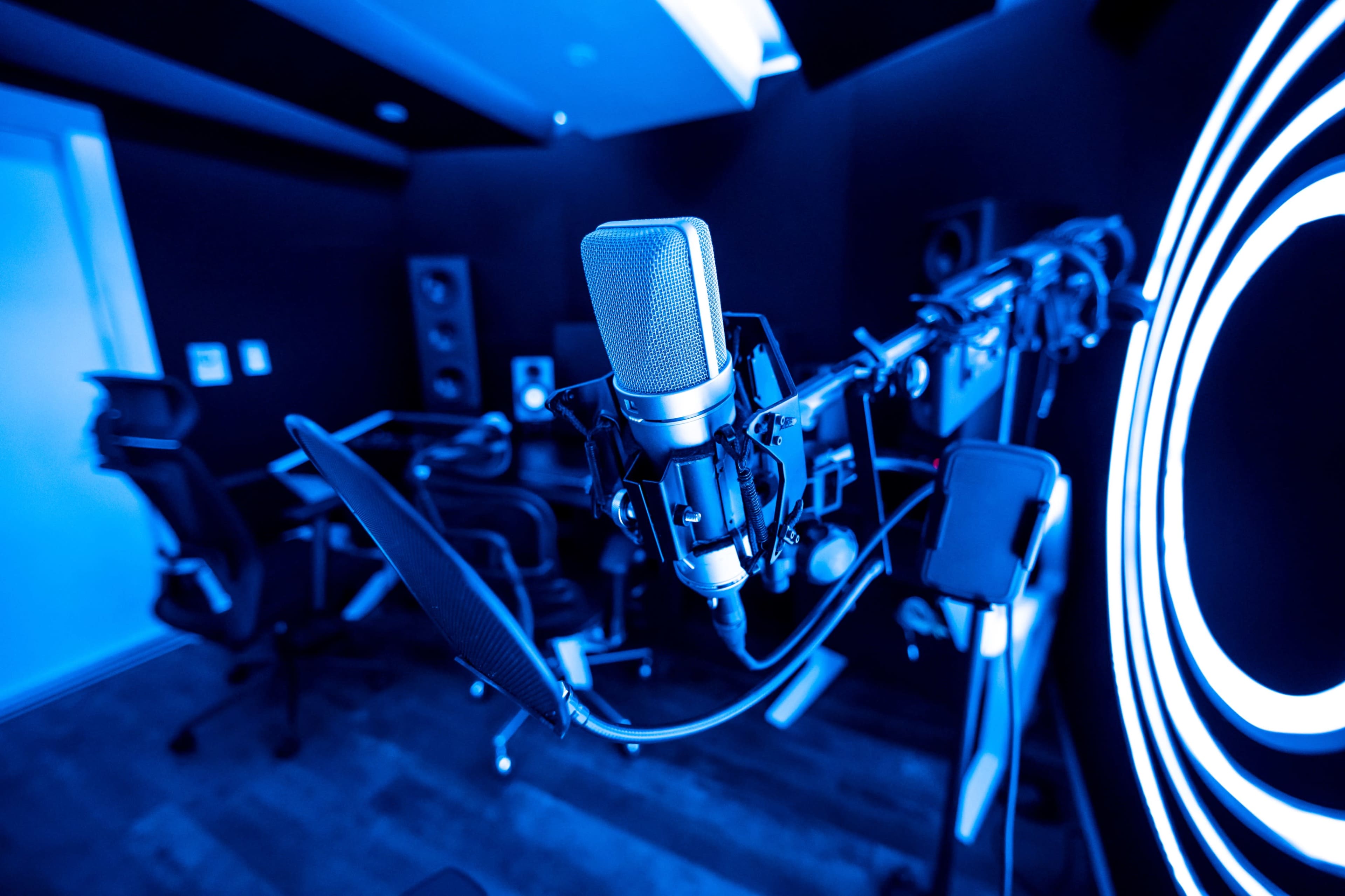 A close-up of a microphone mounted on a stand in a dimly lit recording studio with blue lighting.