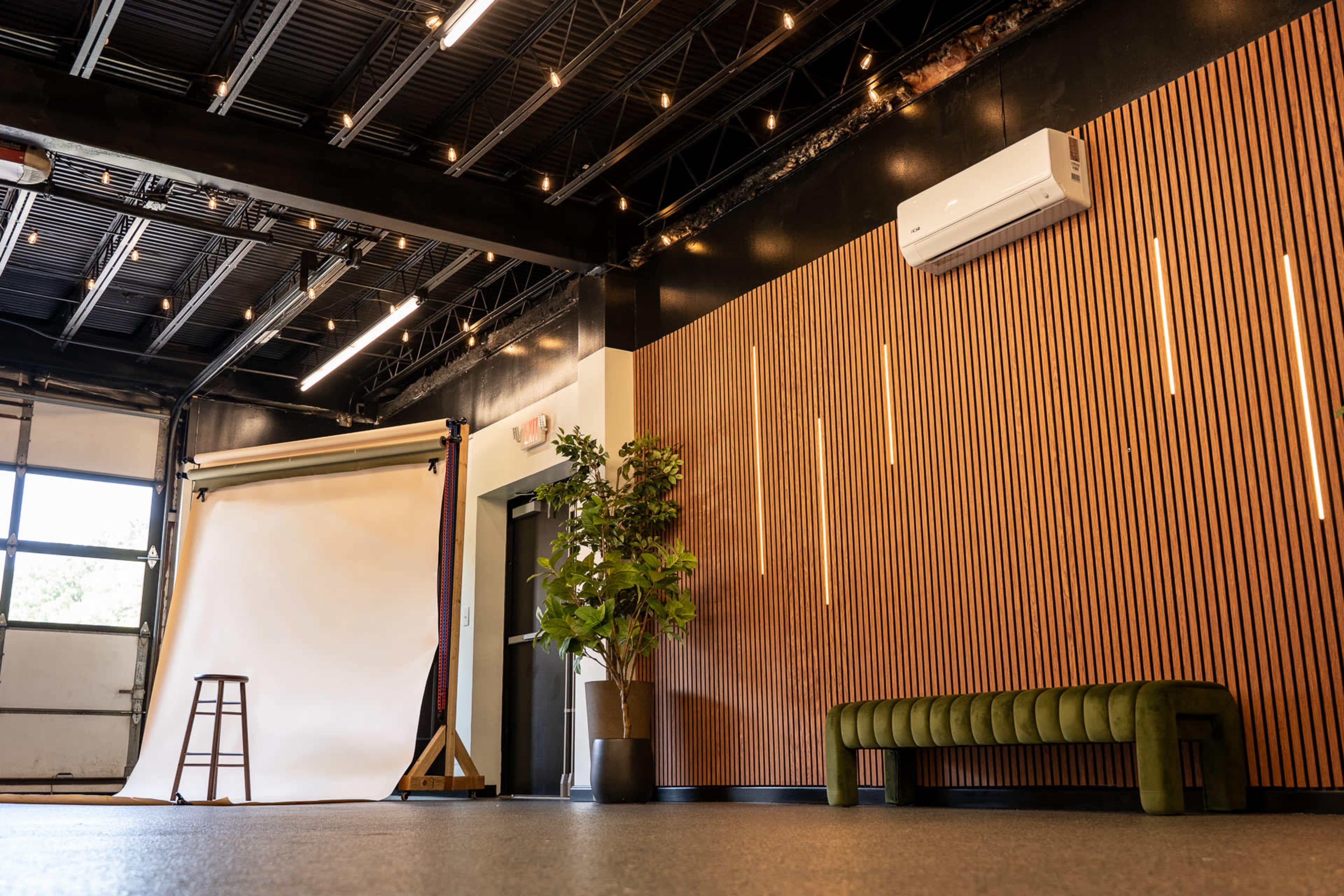 The image shows a spacious, well-lit studio with a backdrop for photography, featuring a green bench, a potted plant, and wooden wall paneling.