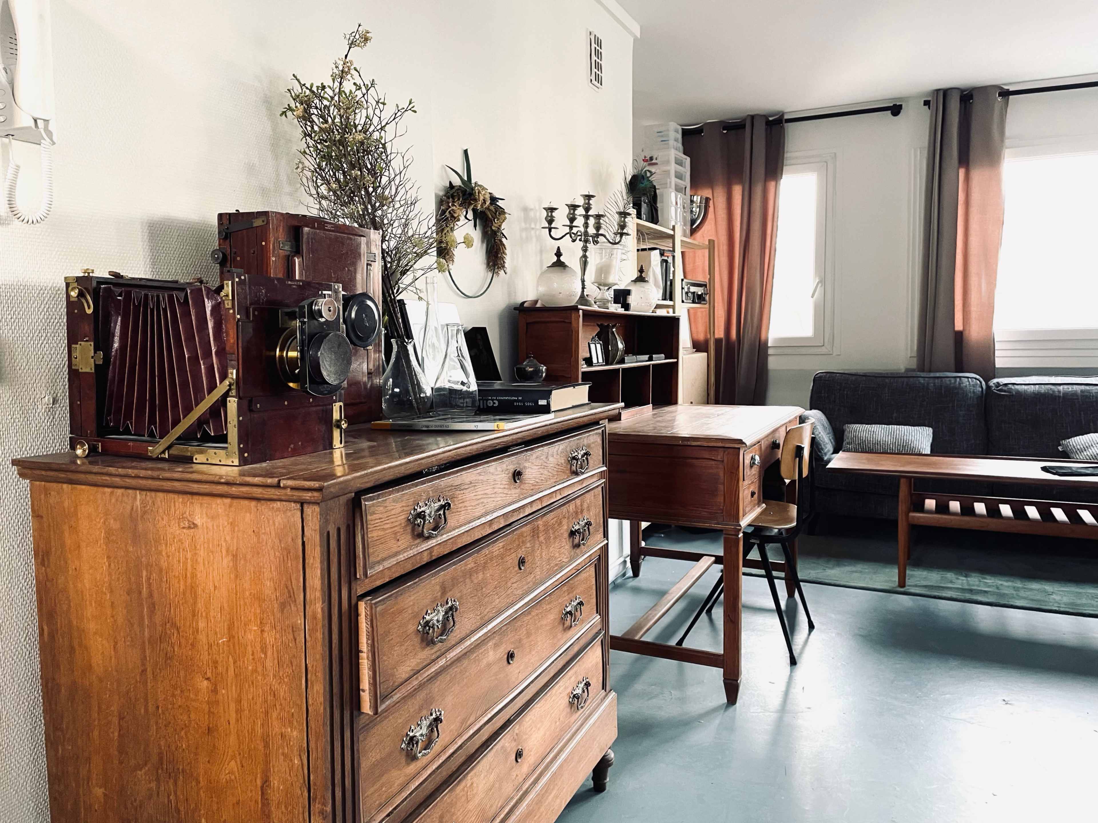 The image shows a living room with a vintage wooden dresser, an antique camera, and a mix of modern and classic furniture.