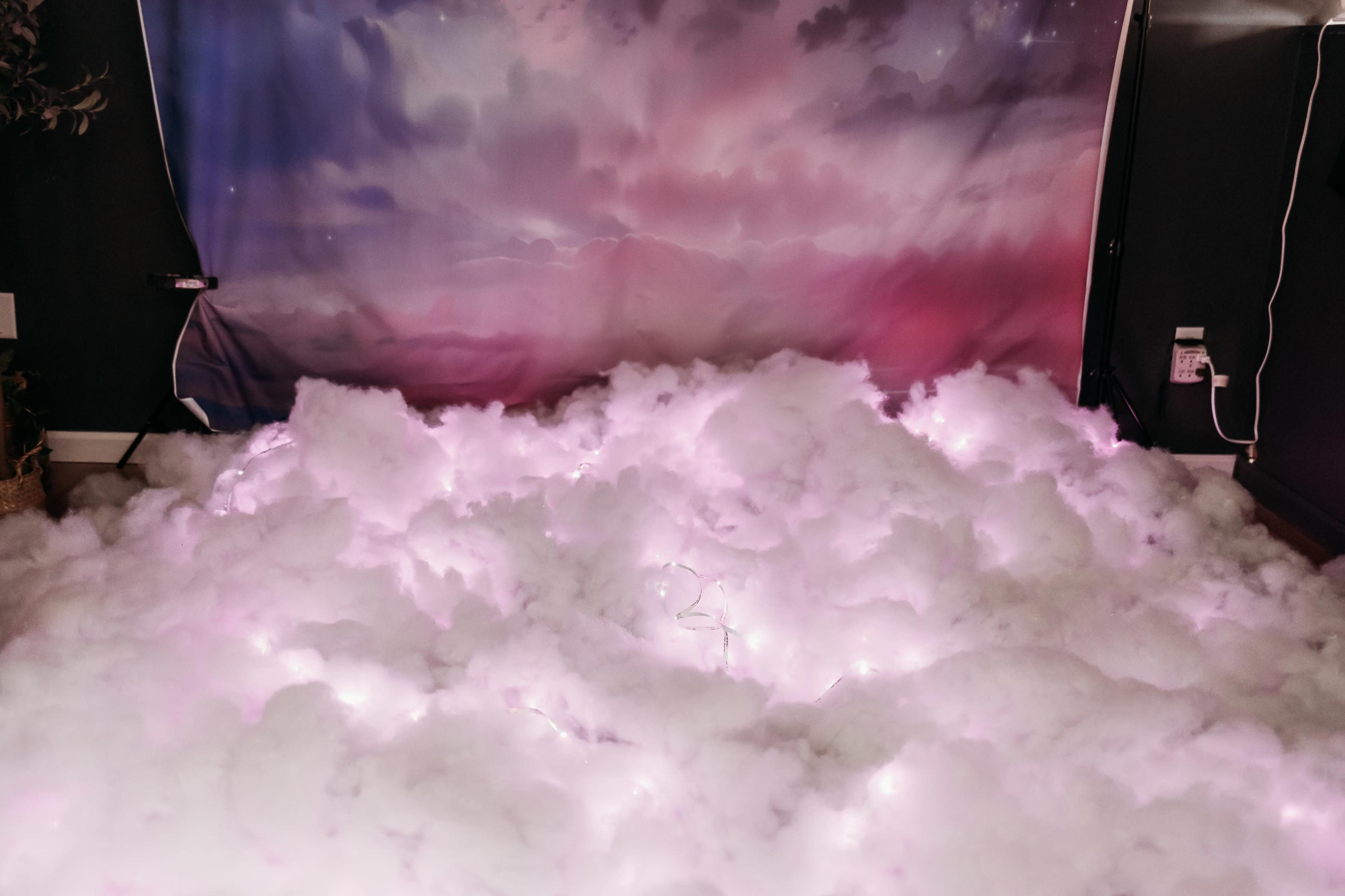 The scene features a backdrop of soft, pink and purple clouds with a floor covered in fluffy white material and illuminated by hidden lights.