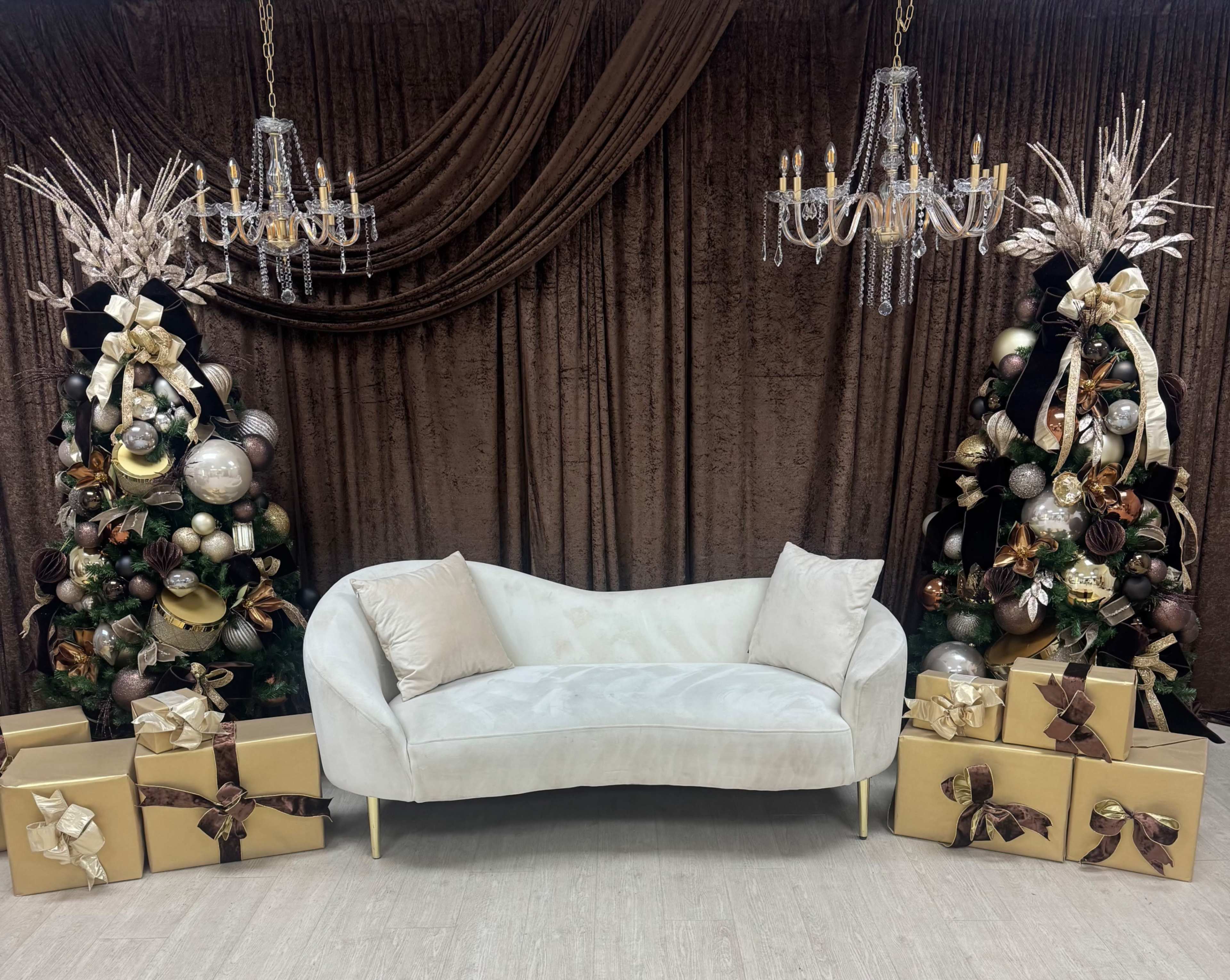 The image features a light-colored curved sofa situated between two elegantly decorated Christmas trees, surrounded by neatly wrapped gift boxes.