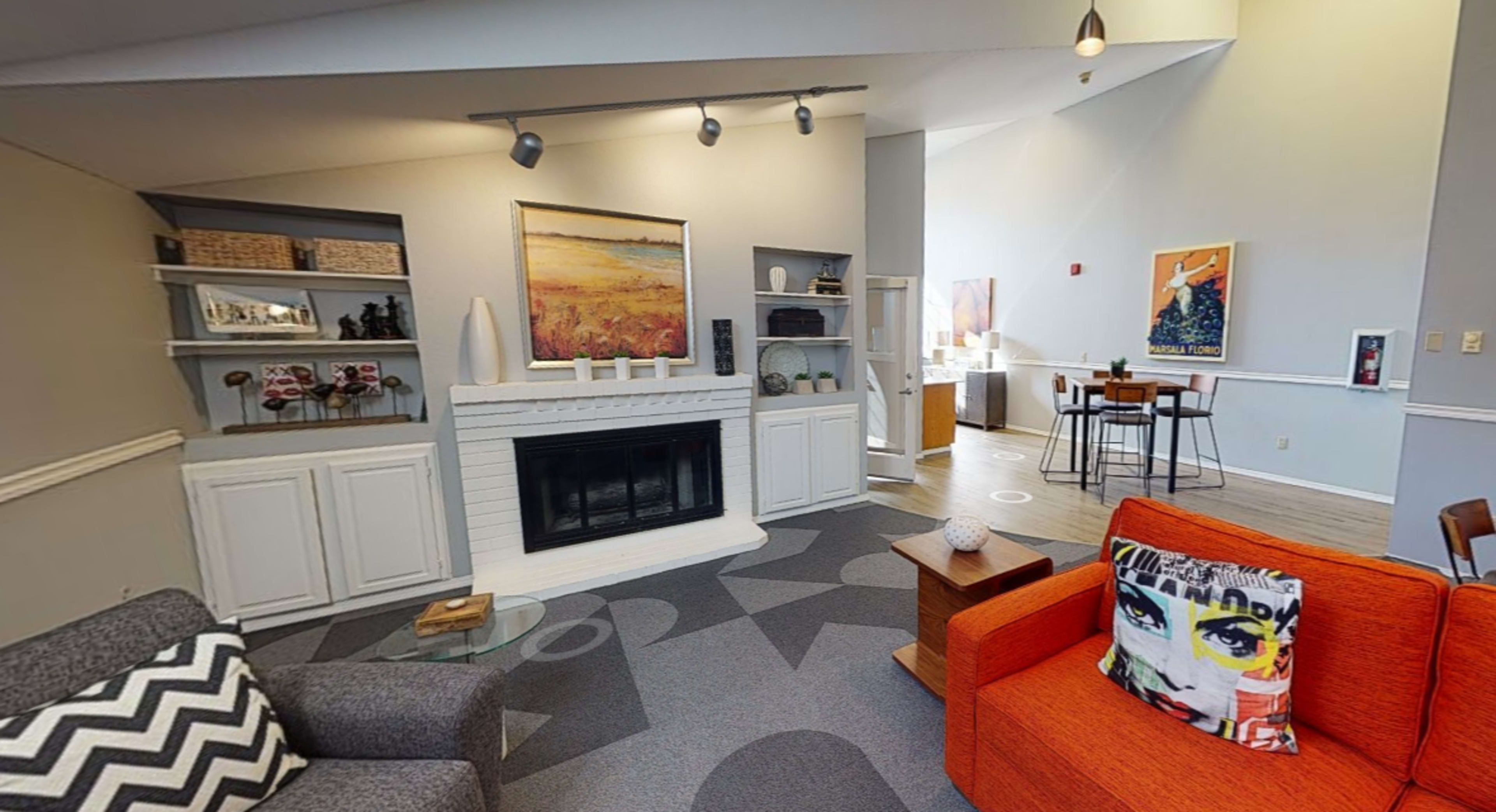 A modern living space with a fireplace, a gray patterned carpet, an orange couch, and various decorative items on shelves.