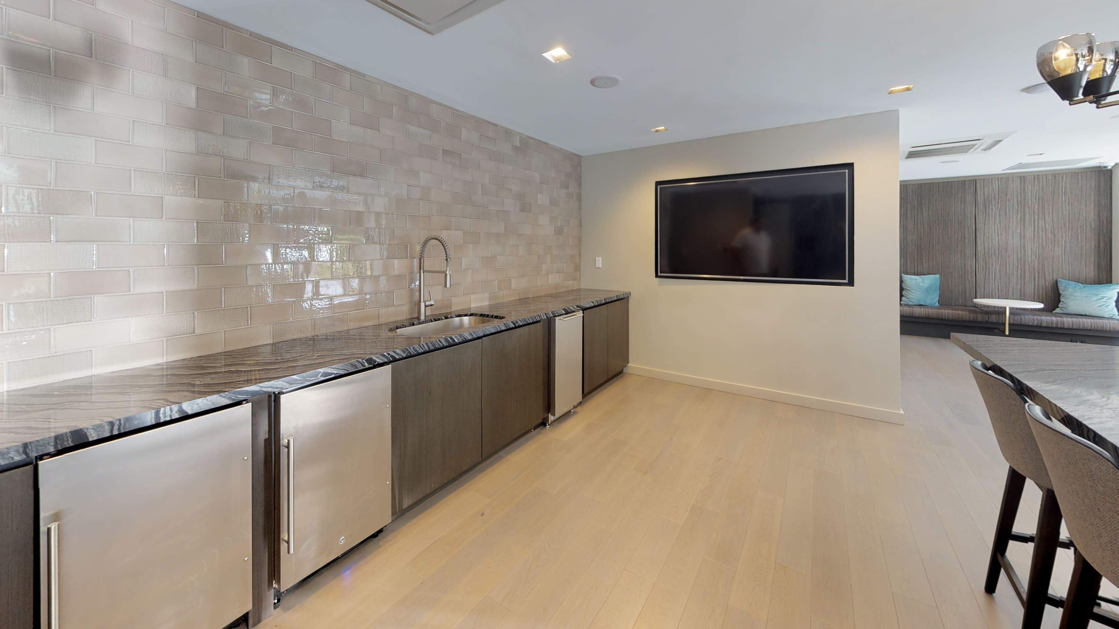 A modern kitchen space features a long countertop with a sink, stainless steel cabinets, and a wall-mounted television.