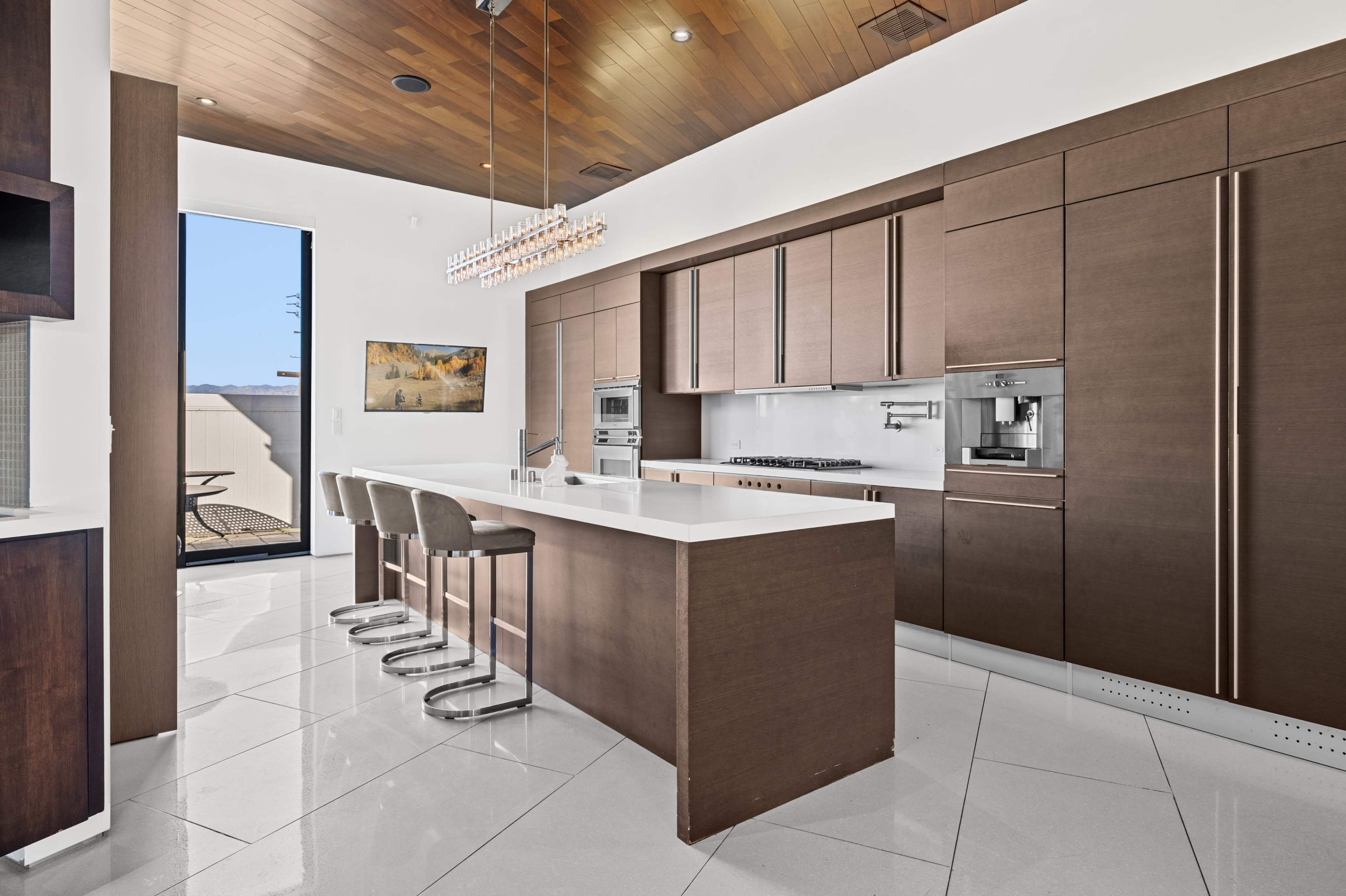 A modern kitchen features wooden cabinetry, a large white island with barstools, and a window providing natural light.