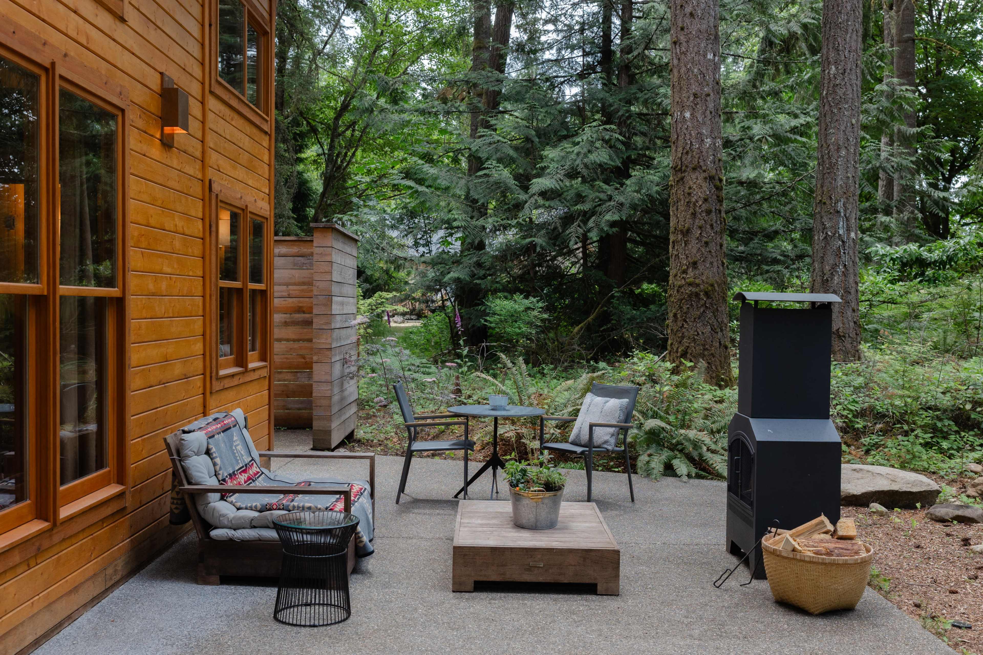 A wooden patio features a small seating area with a table and chairs, surrounded by trees and greenery.