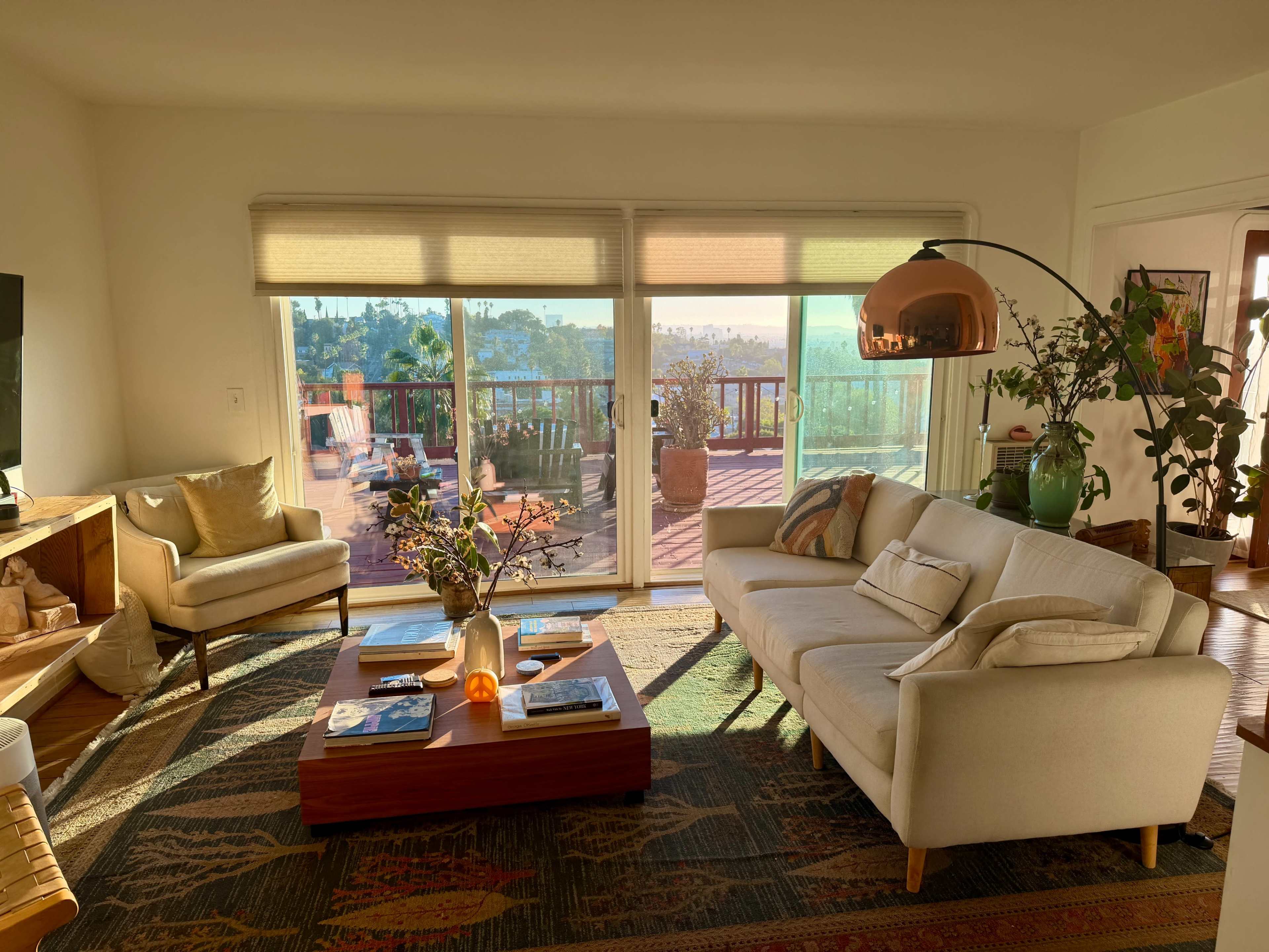 A modern living room features a white sofa, a wooden coffee table with books, and large glass doors that open to a sunny outdoor deck.