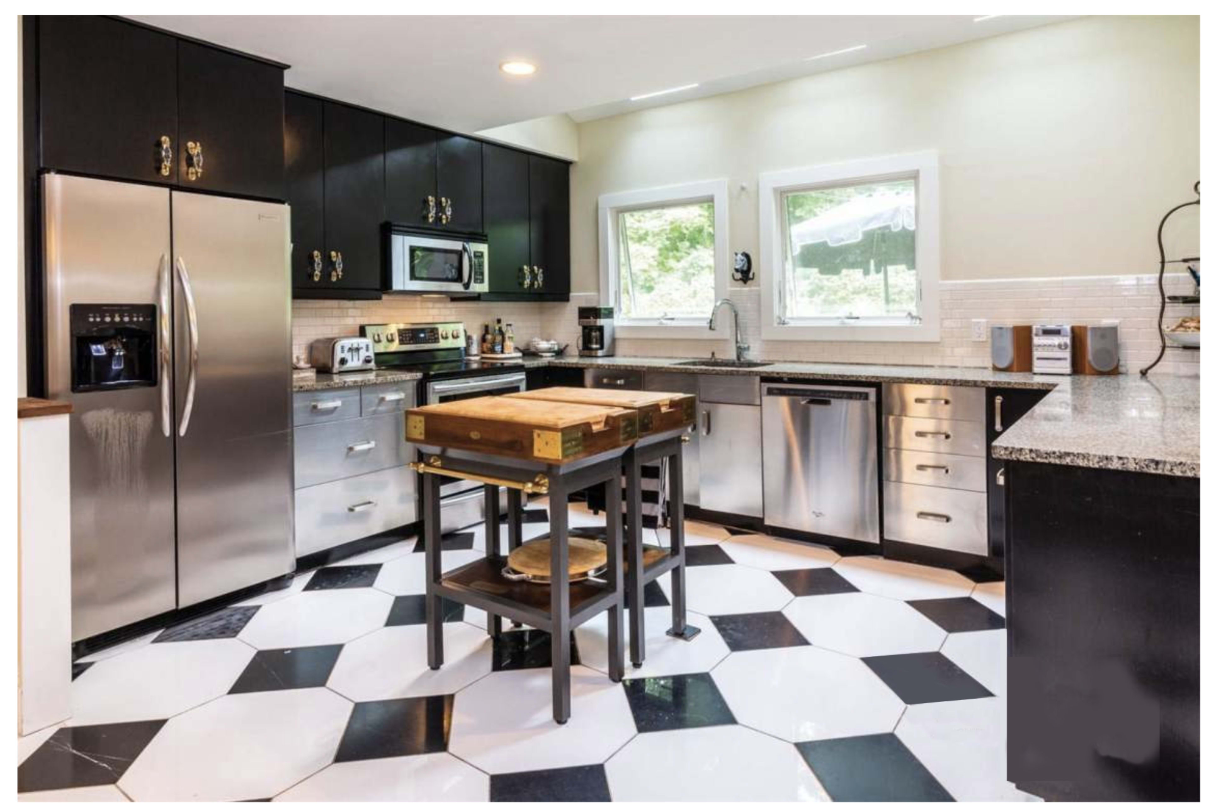 The kitchen features black cabinetry, stainless steel appliances, and a hexagonal black-and-white tiled floor with a central wooden island.