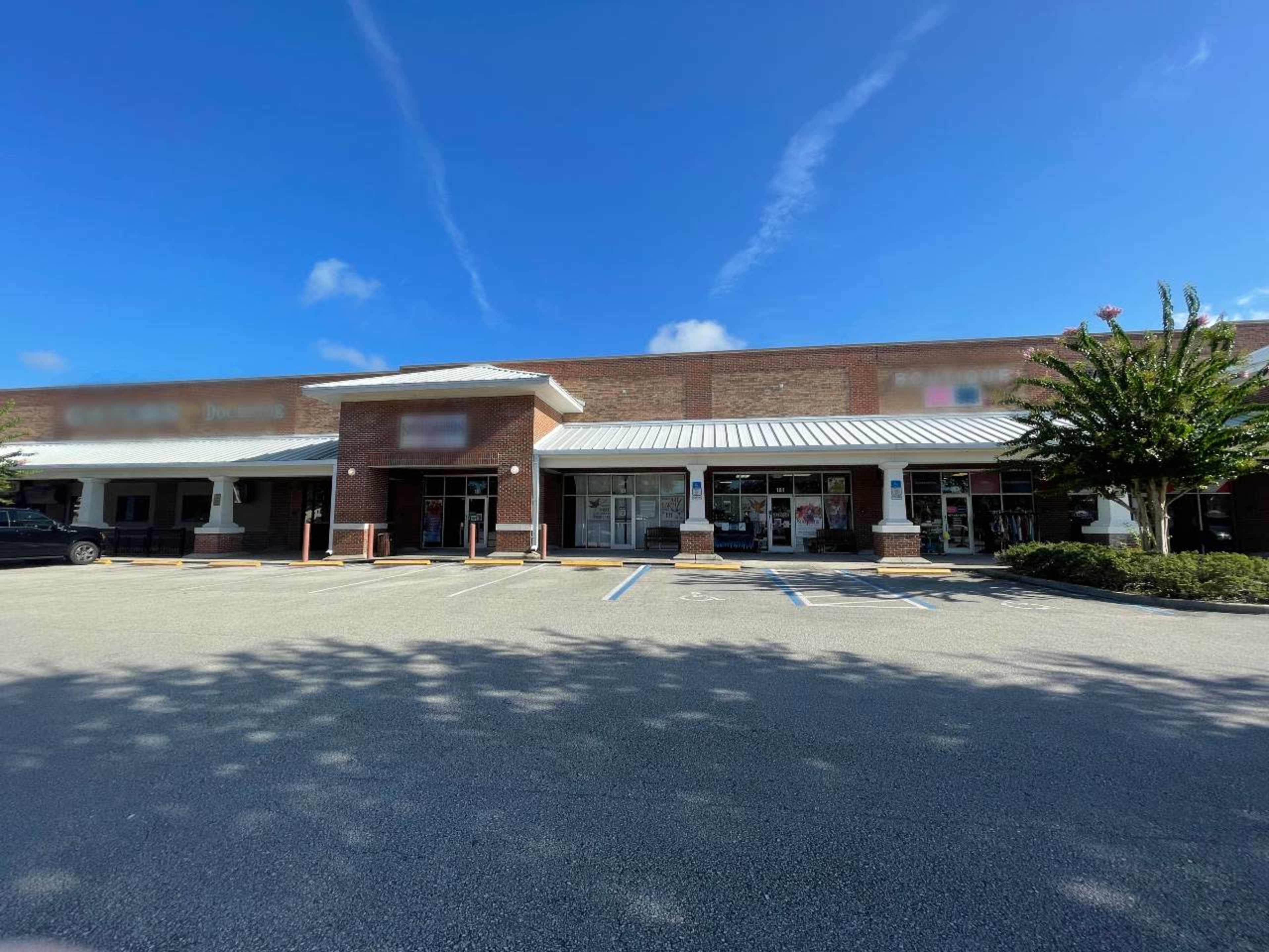 A retail building with a brick facade and a white roof, surrounded by a parking lot under a clear blue sky.