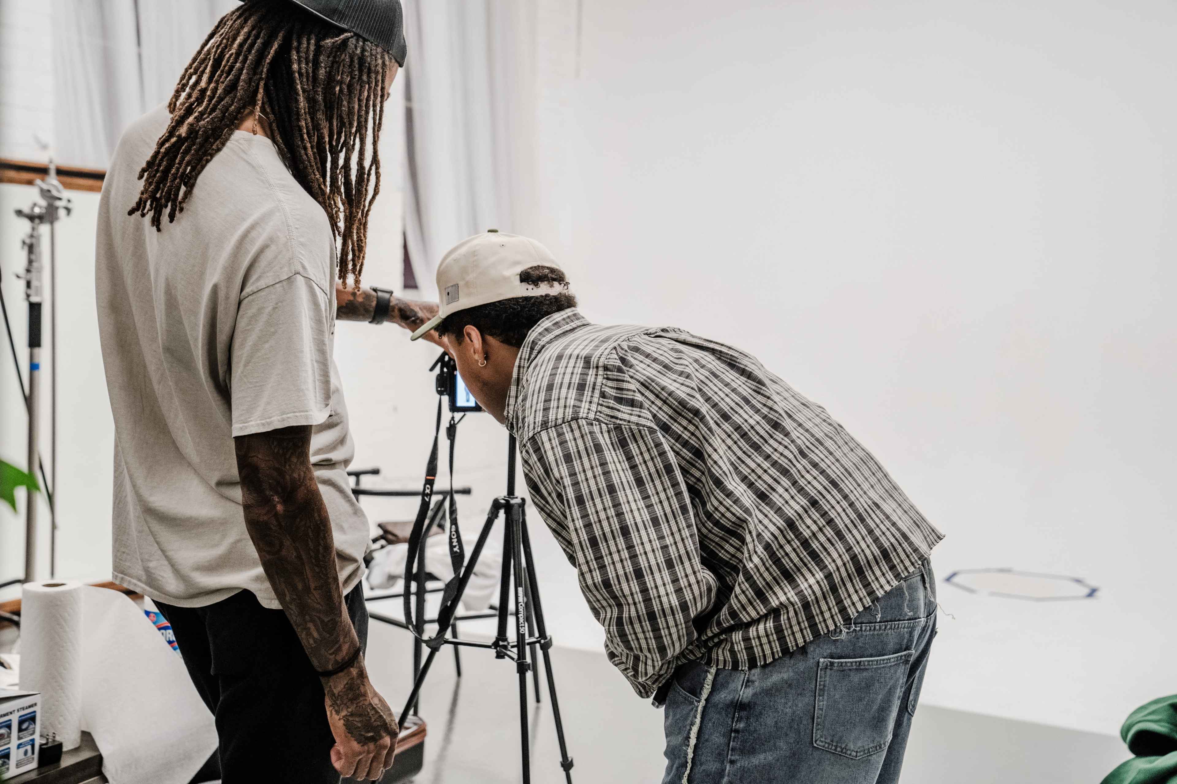 Two individuals are examining the display of a camera on a tripod in a photography studio.