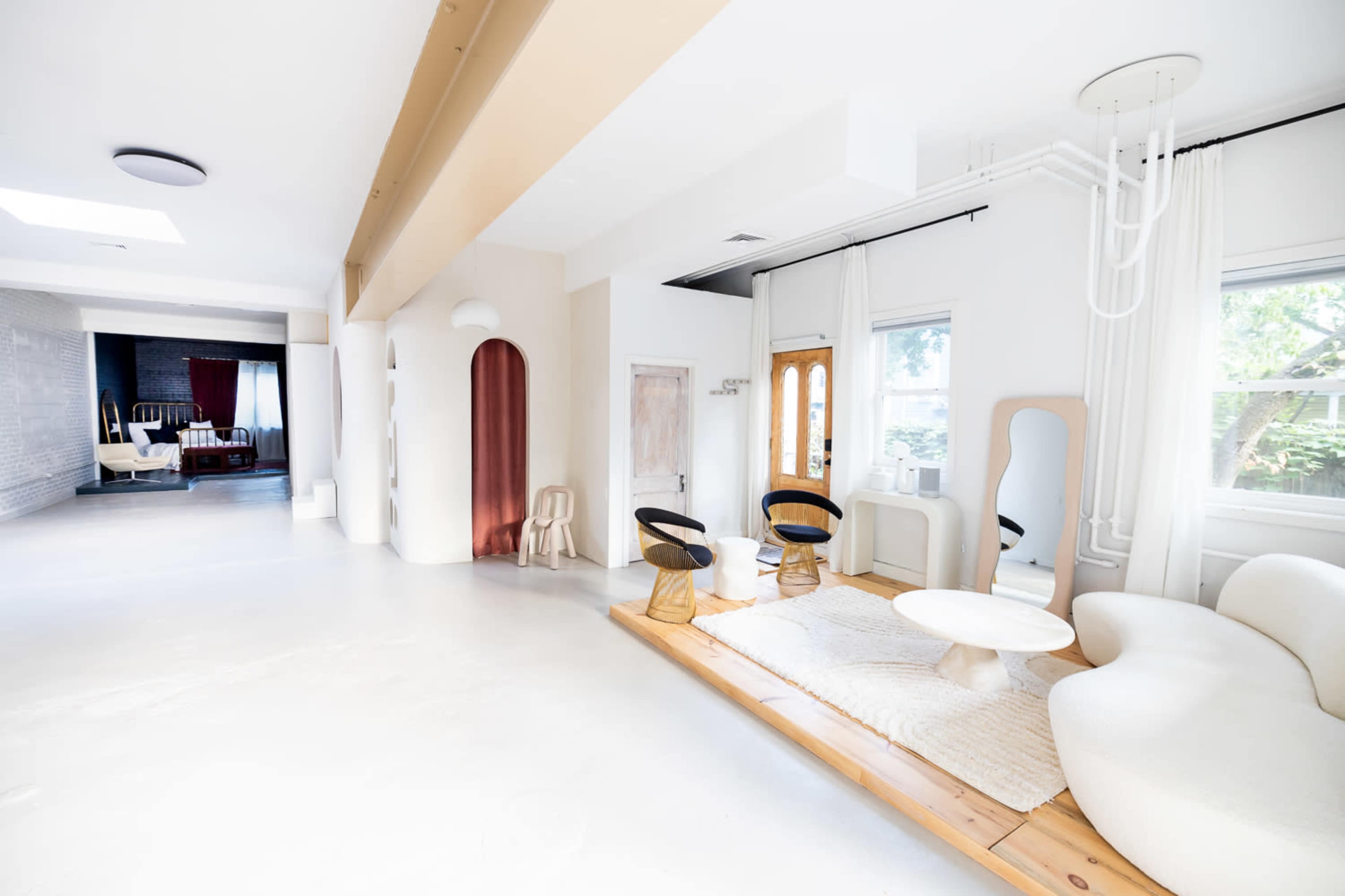 A spacious, modern interior with minimalist furniture, including a curved sofa and circular table, set against light-colored walls and large windows.