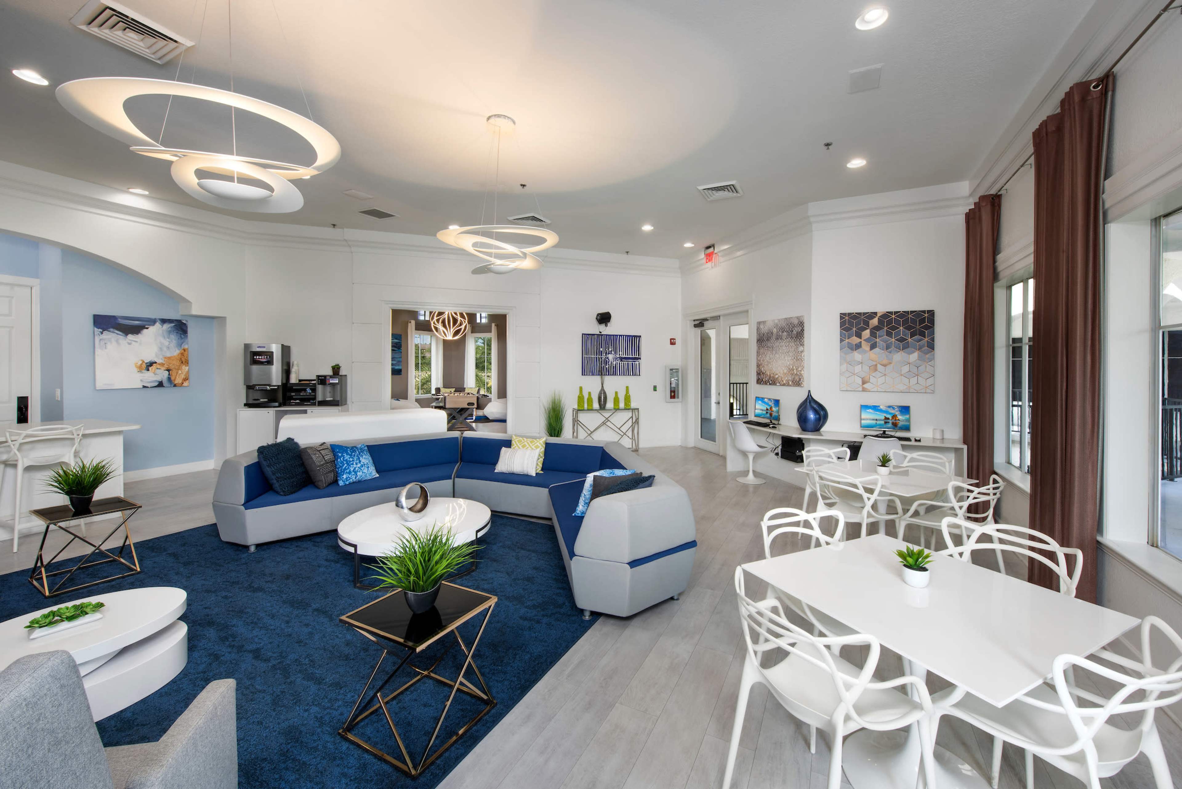 The image shows a modern lounge area featuring a blue and gray sectional sofa, circular light fixtures, and a mix of seating arrangements, including tables and chairs.