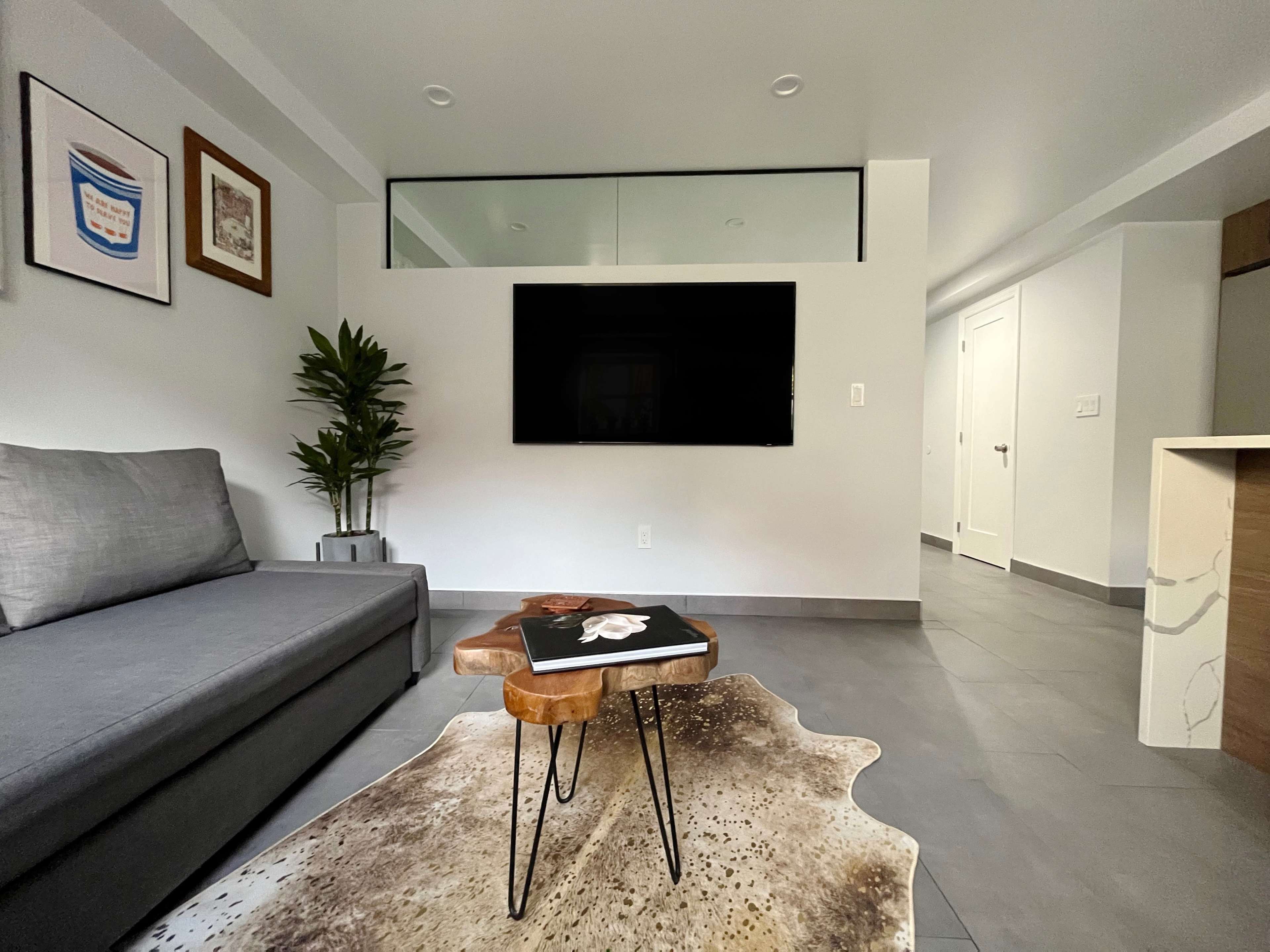 A modern living room featuring a gray sofa, a small wooden table with a book, and a large flat-screen TV mounted on the wall.