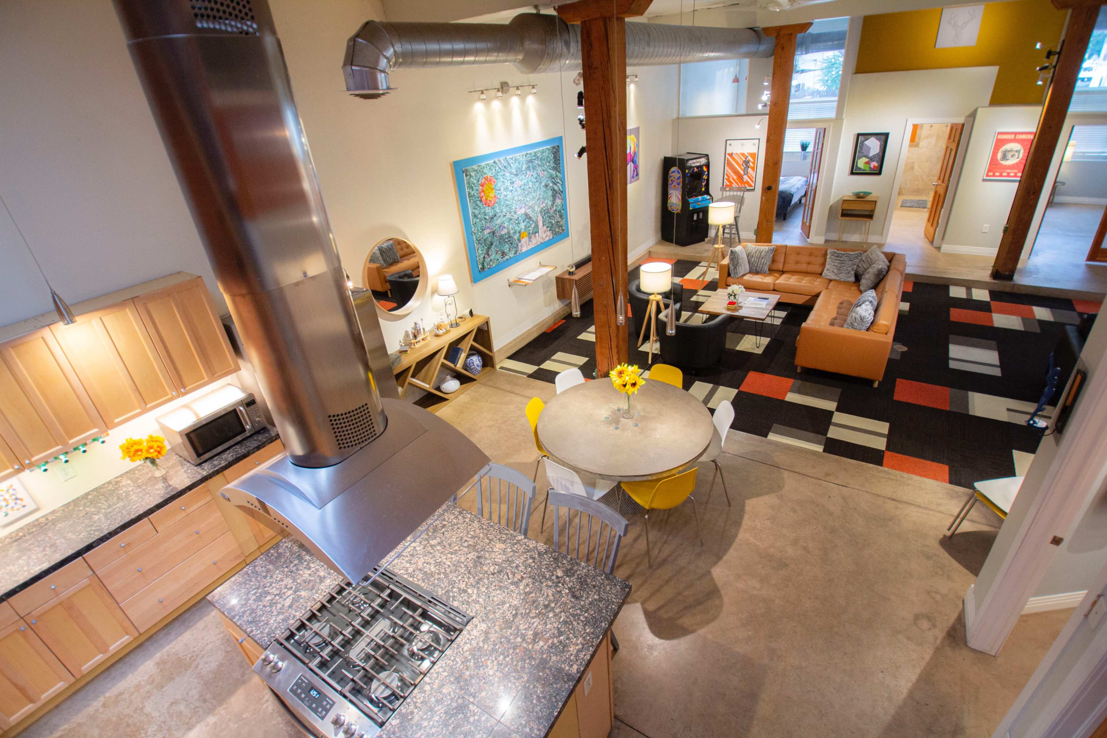 An open-concept living space features a kitchen with a large island, a dining area with a circular table, and a lounge area with a sofa and colorful artwork on the walls.