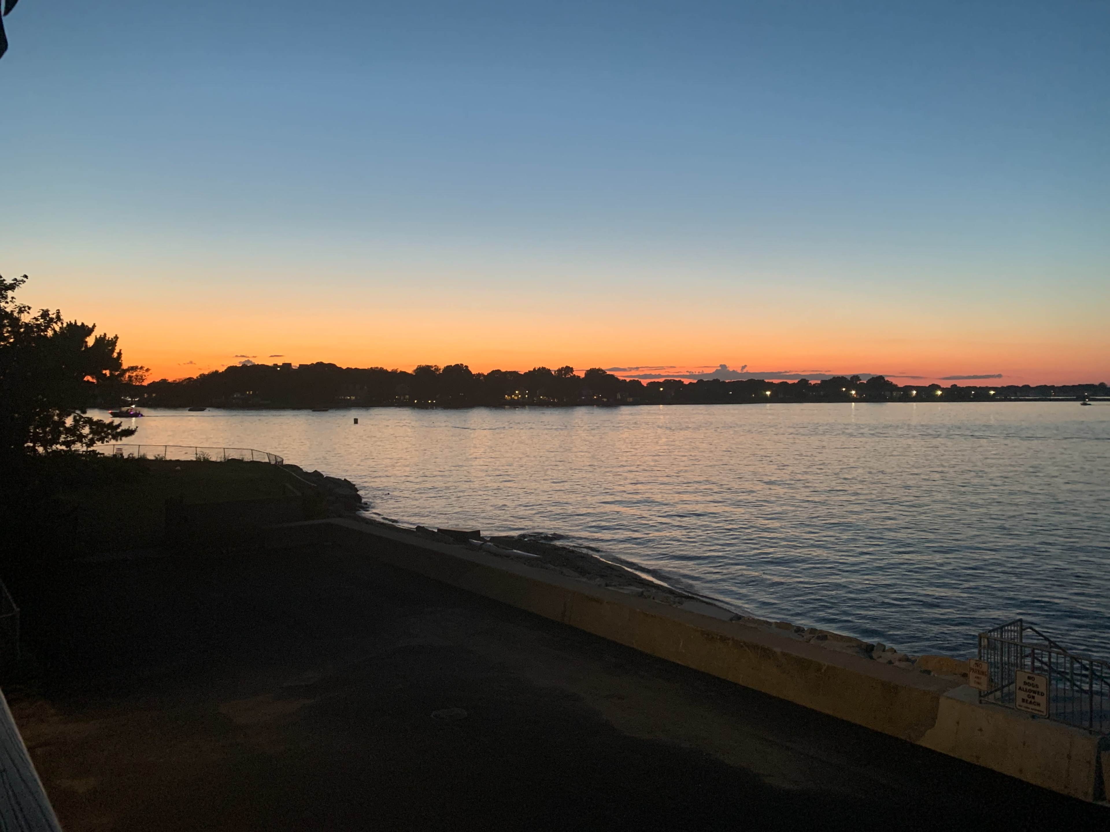 The image shows a tranquil waterfront at sunset, with orange and blue hues reflected on the water.