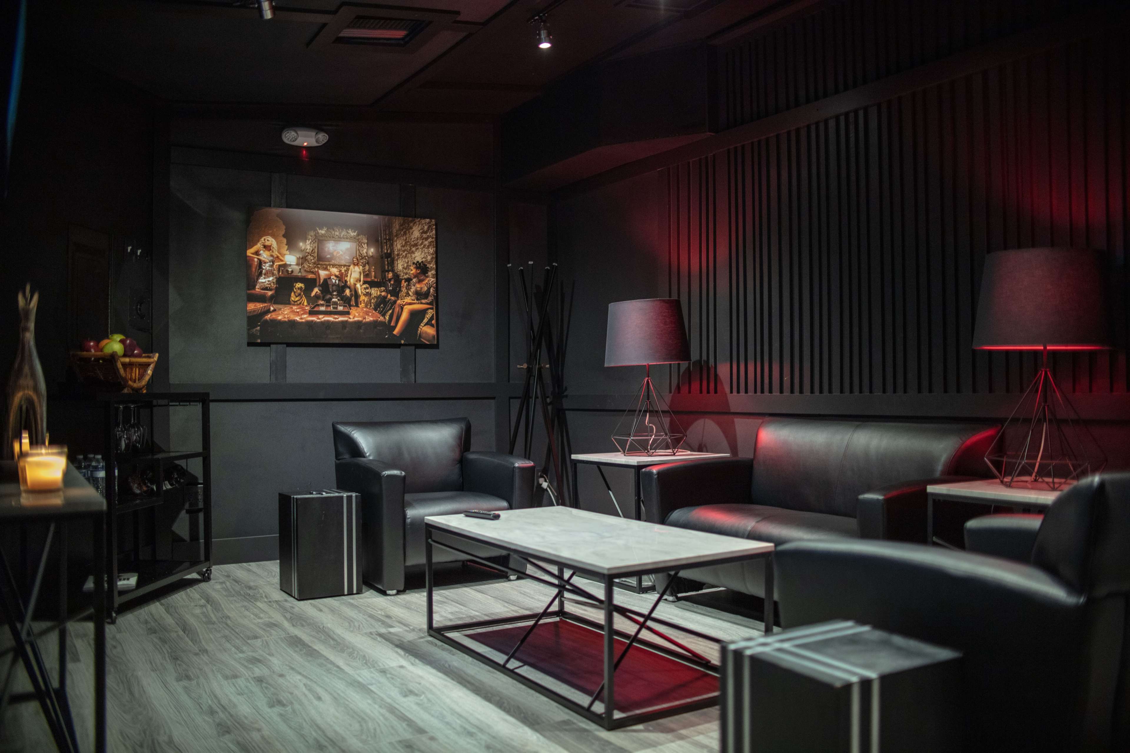 A modern lounge area with black leather furniture, a coffee table, and wall art, illuminated by table lamps.