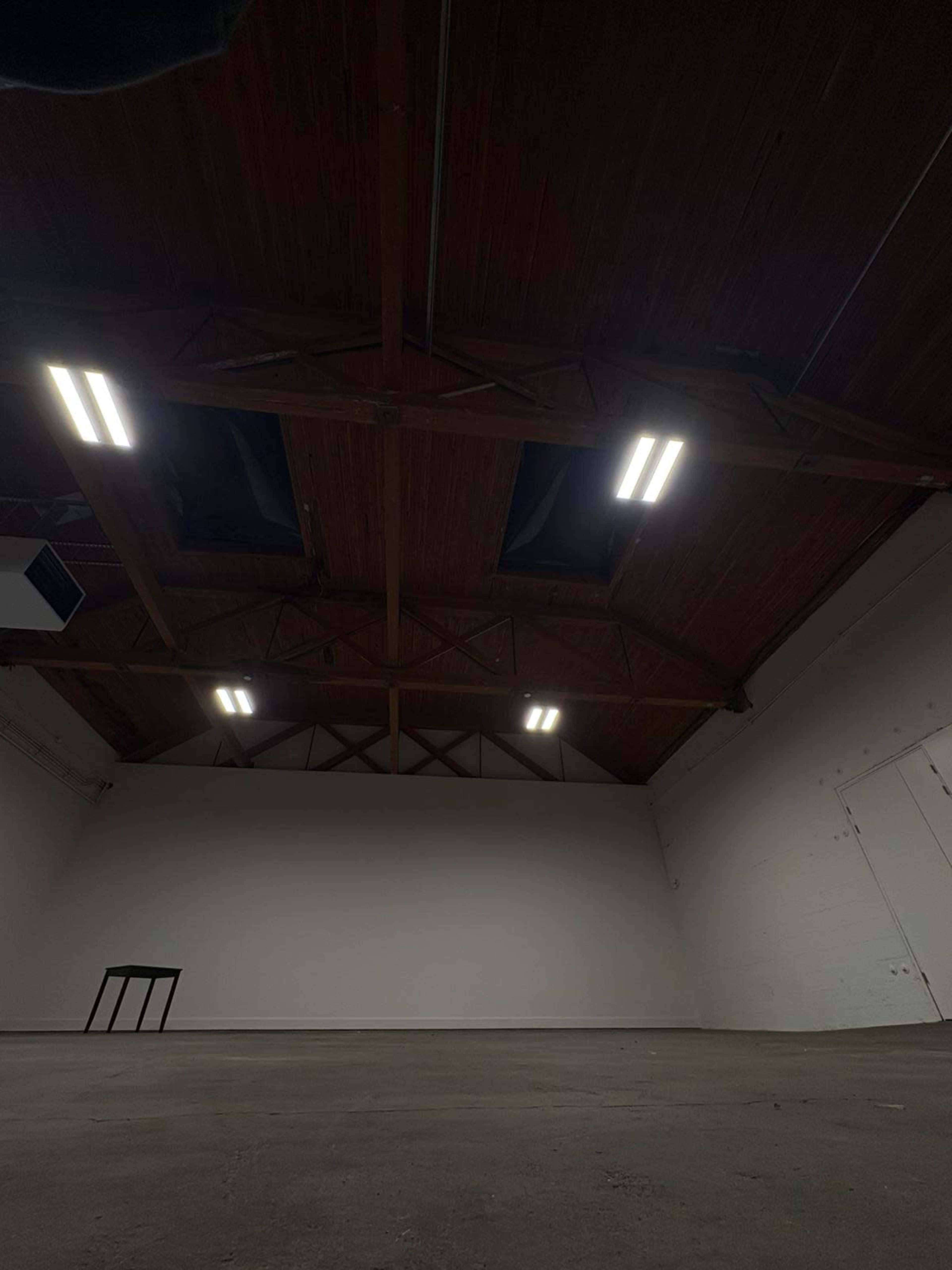 The image shows the interior of an empty industrial space with wooden beams and bright overhead lighting.
