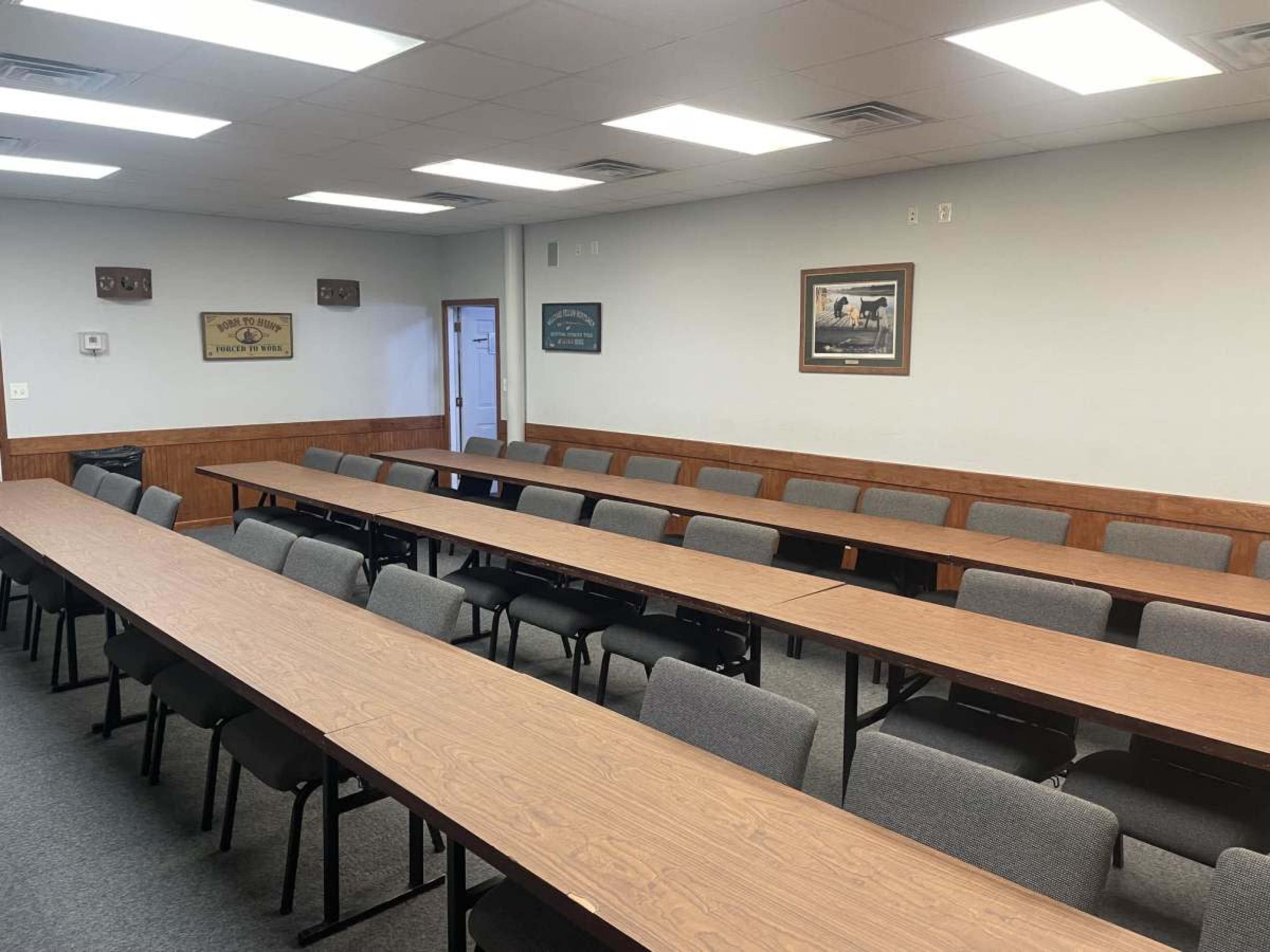 The image shows a conference room with several rows of long tables and chairs arranged in a grid pattern.