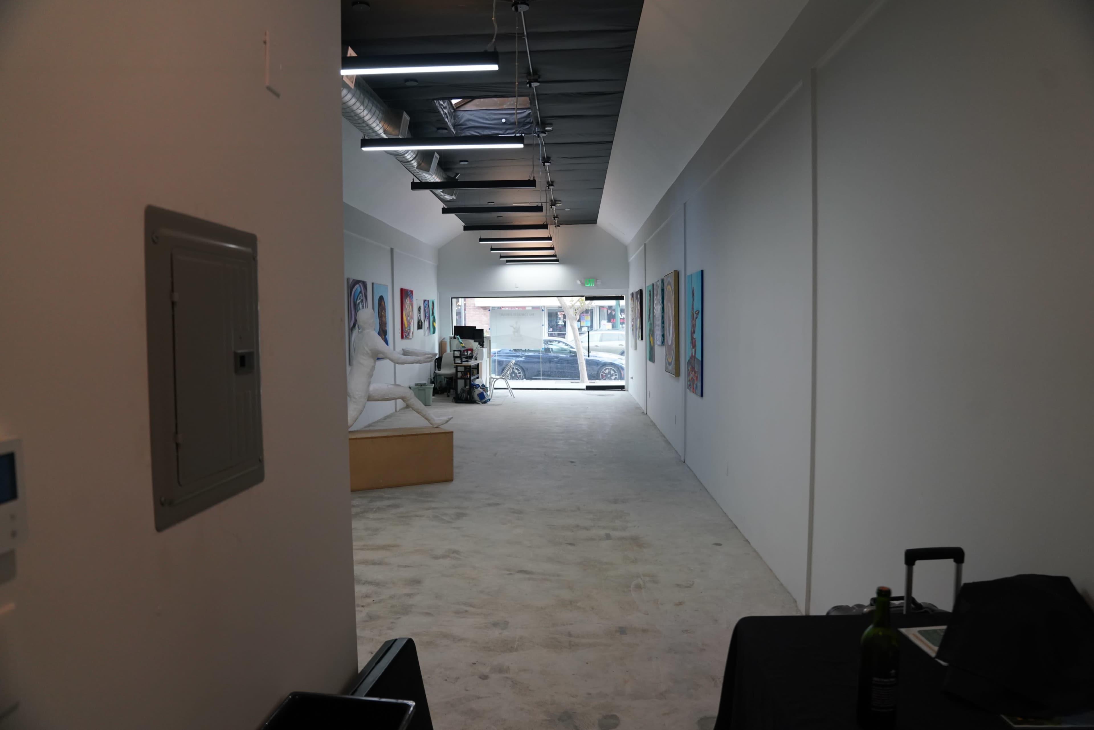 A long, narrow white corridor features artwork on the walls, leading to a large window at the far end.