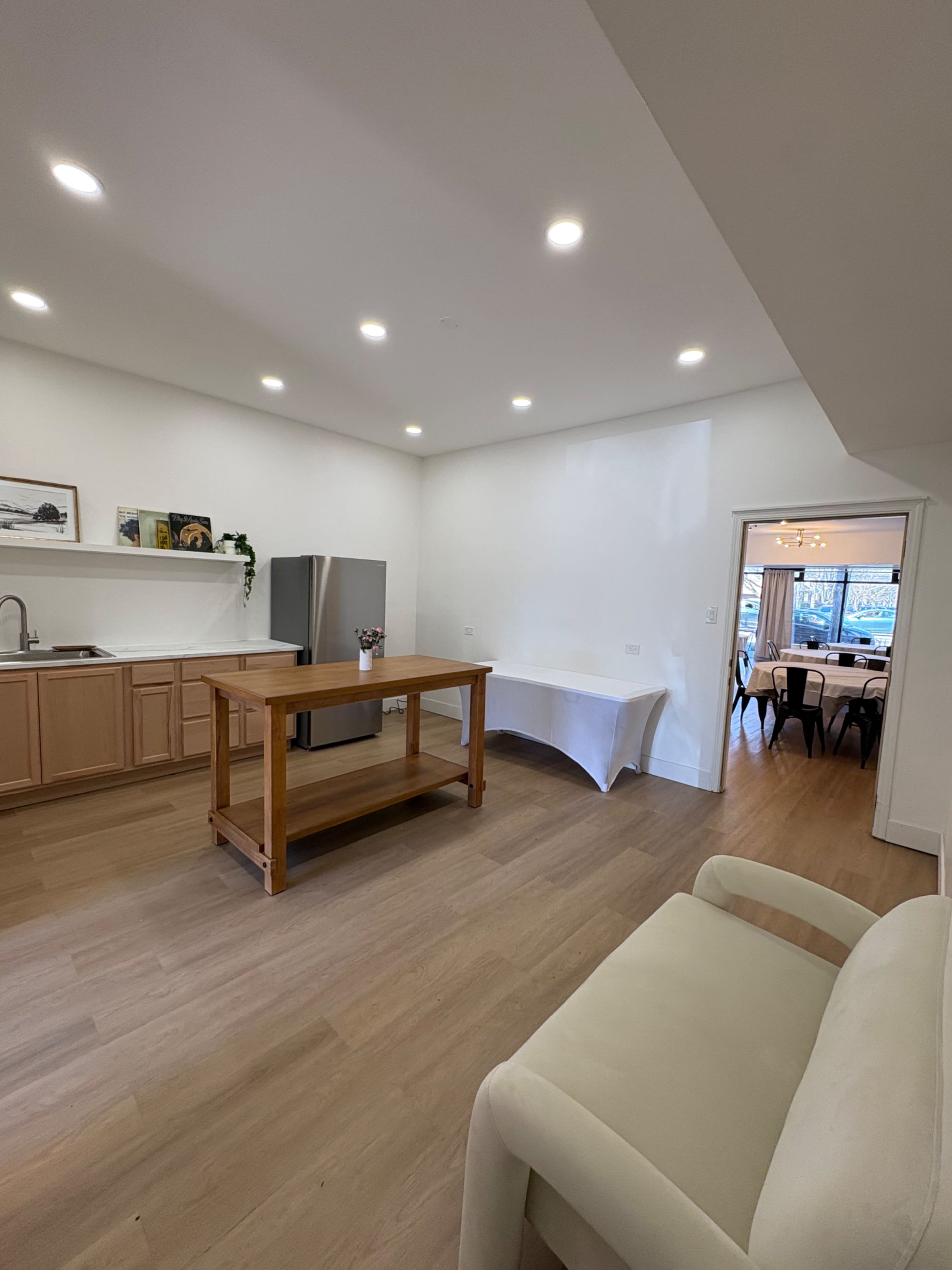 The image shows a modern kitchen with wooden cabinets, a central wooden island, stainless steel appliances, and a dining area visible through an open doorway.