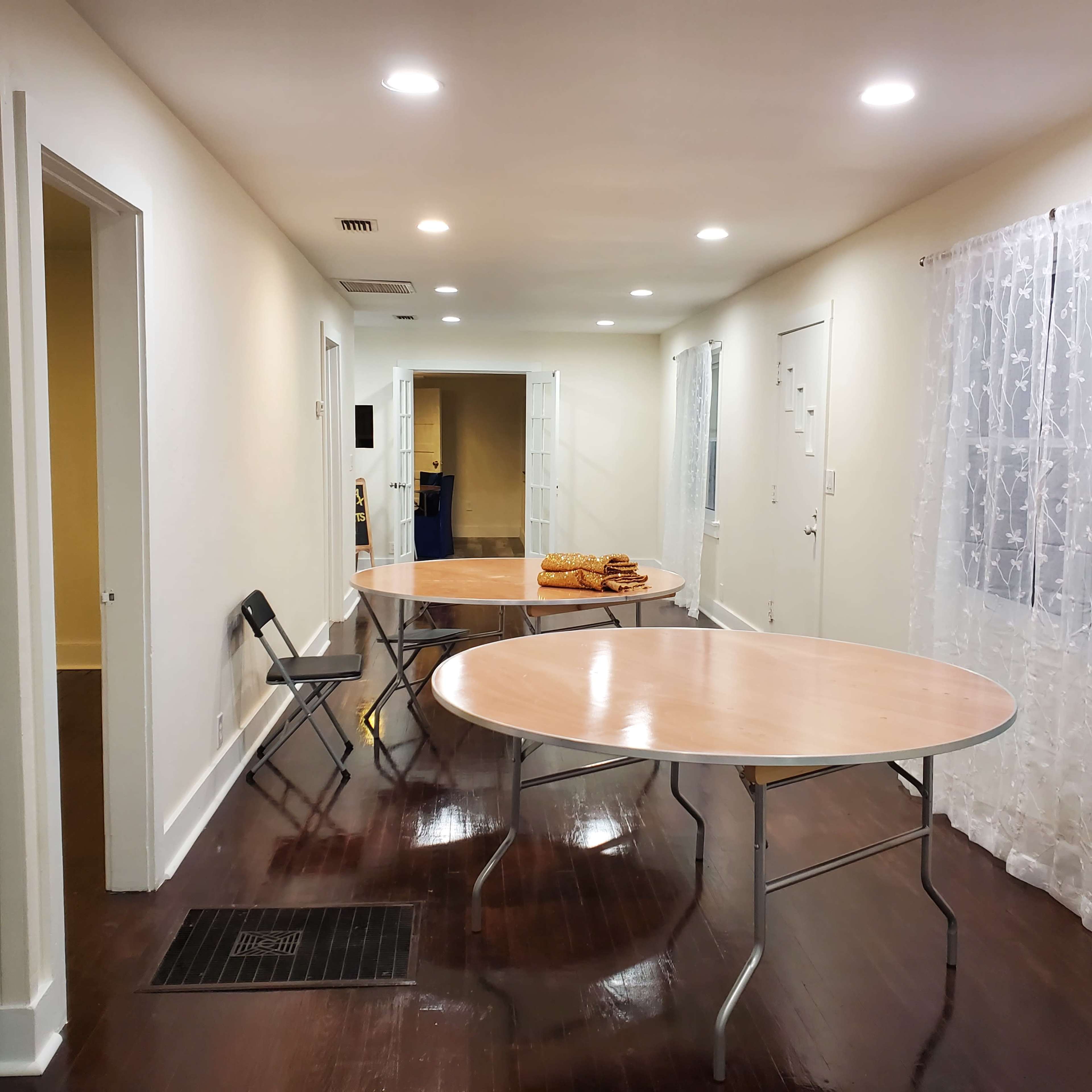 A well-lit room with two round tables, one with a stack of bread, and doors leading to other areas.