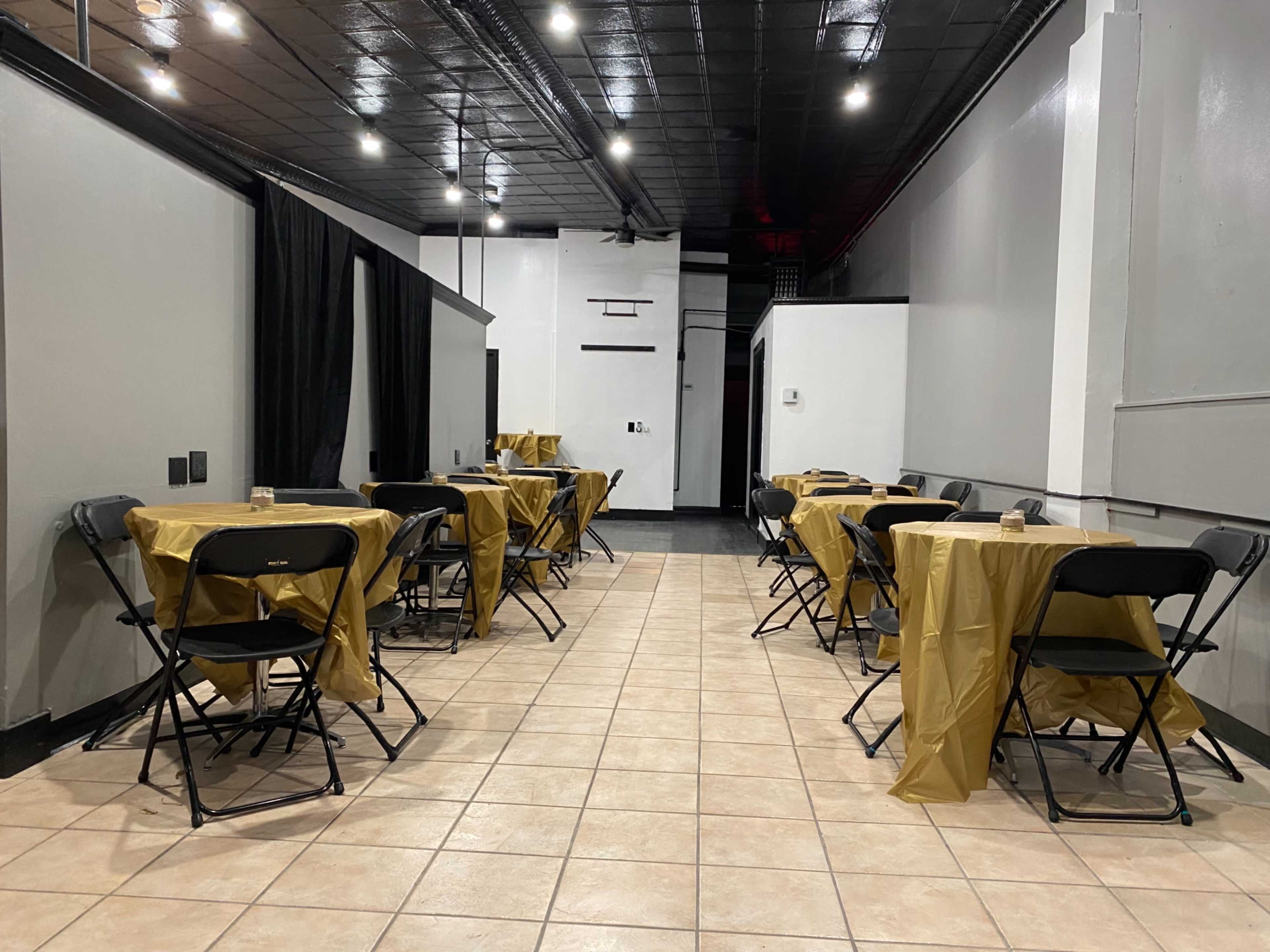 A long, narrow room with tables covered in golden tablecloths and black folding chairs arranged on either side.