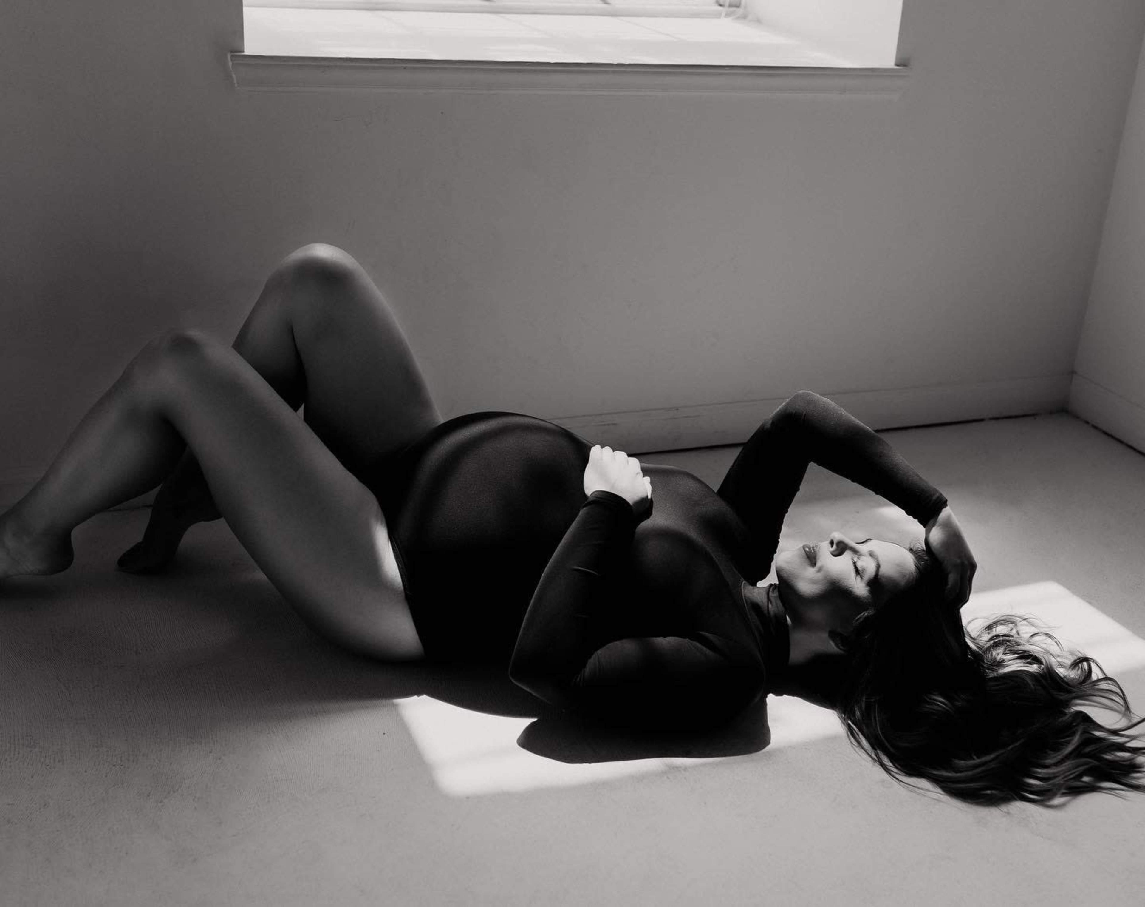 A pregnant woman lies on her side in a sunlit room, with her hand resting on her belly and her hair spread on the floor.