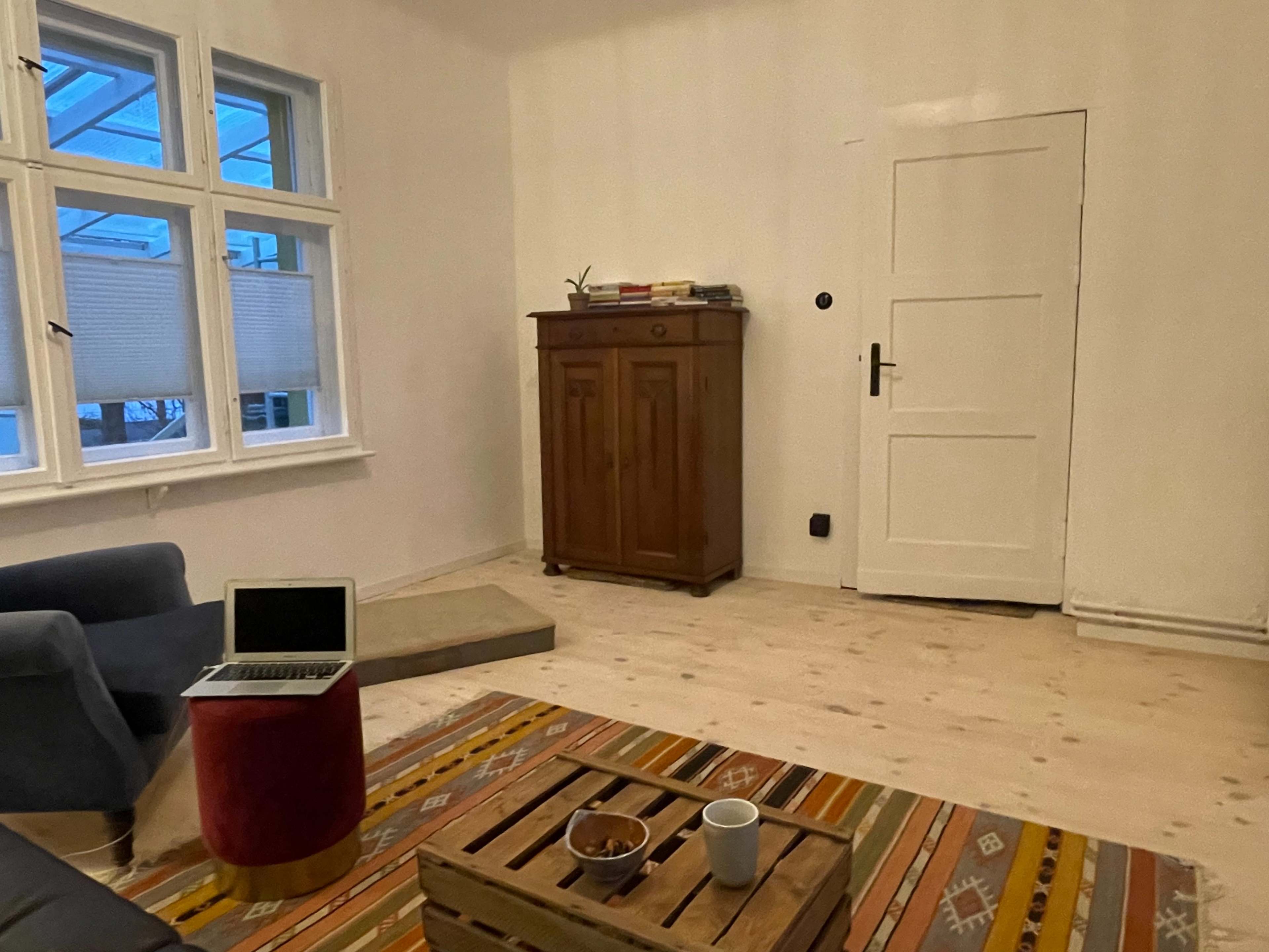 A simple, unfurnished room with a wooden floor, a blue sofa, a small red table, a wooden cabinet, and a door.