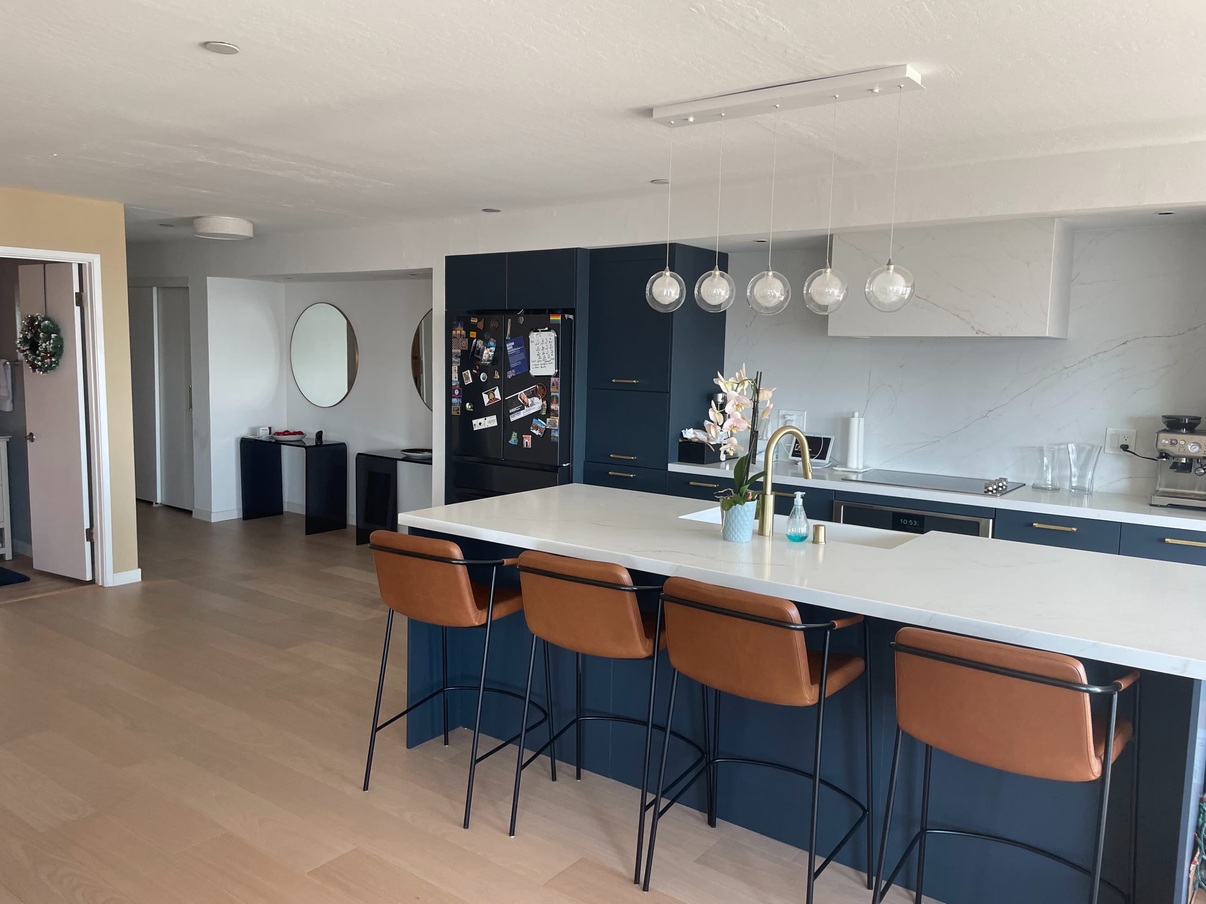 A modern kitchen with a large island, four brown bar stools, and a minimalist decor featuring a black refrigerator and a plant centerpiece.