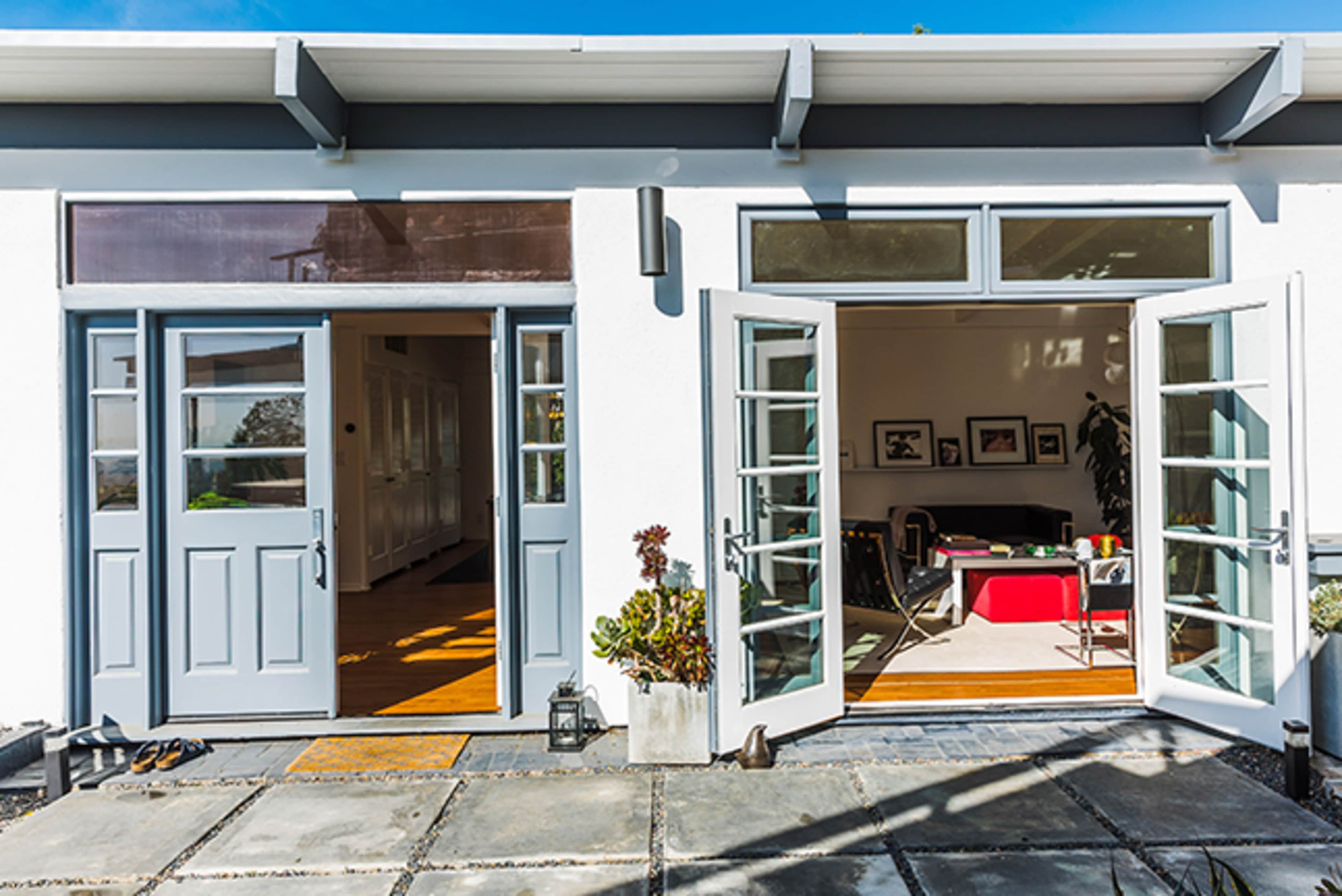 Two double doors open to an interior space with a view of a room featuring colorful furniture and large windows.