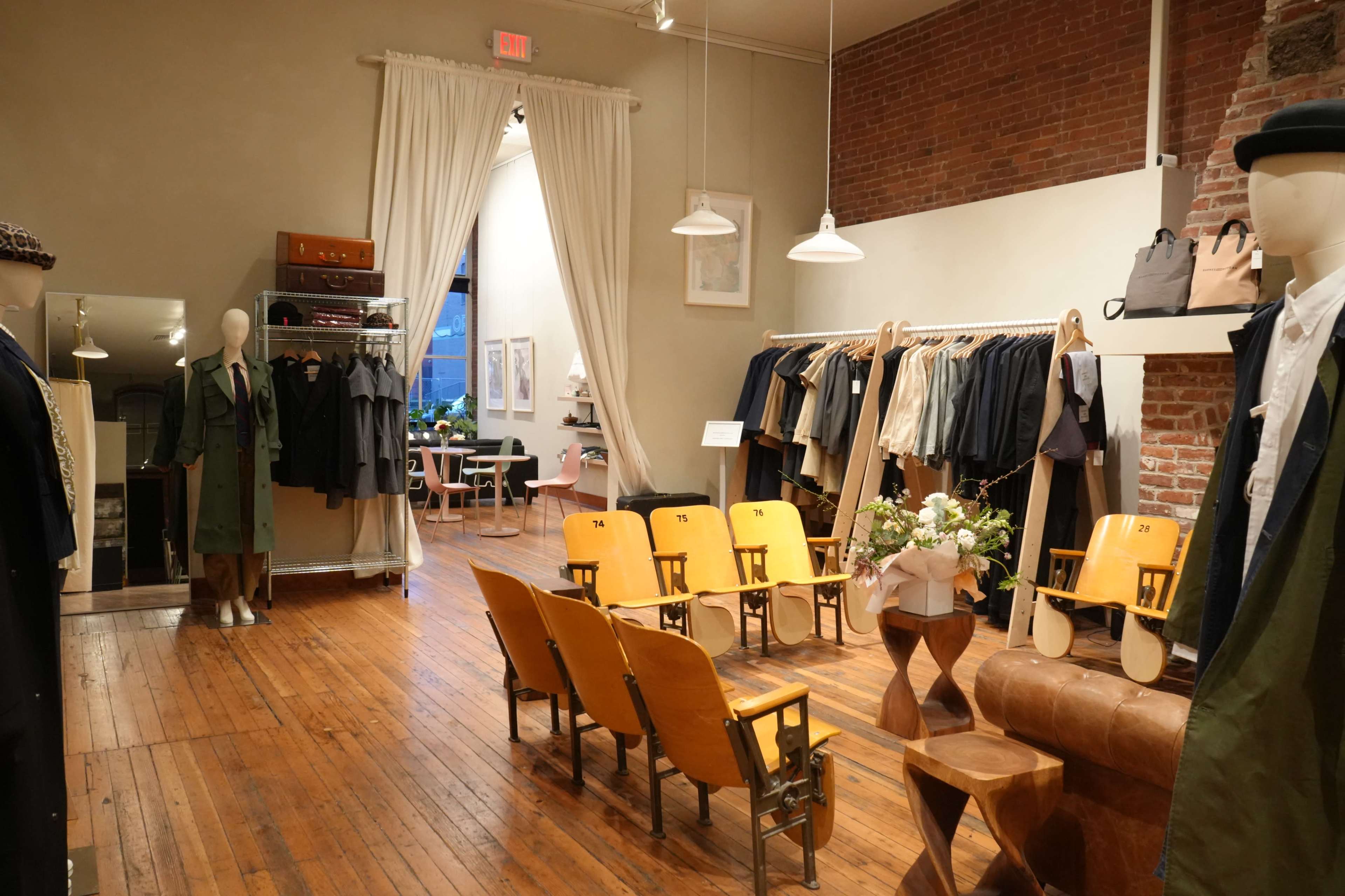 The image shows a clothing store with wooden floors, brick walls, and display mannequins surrounded by seating and tables.
