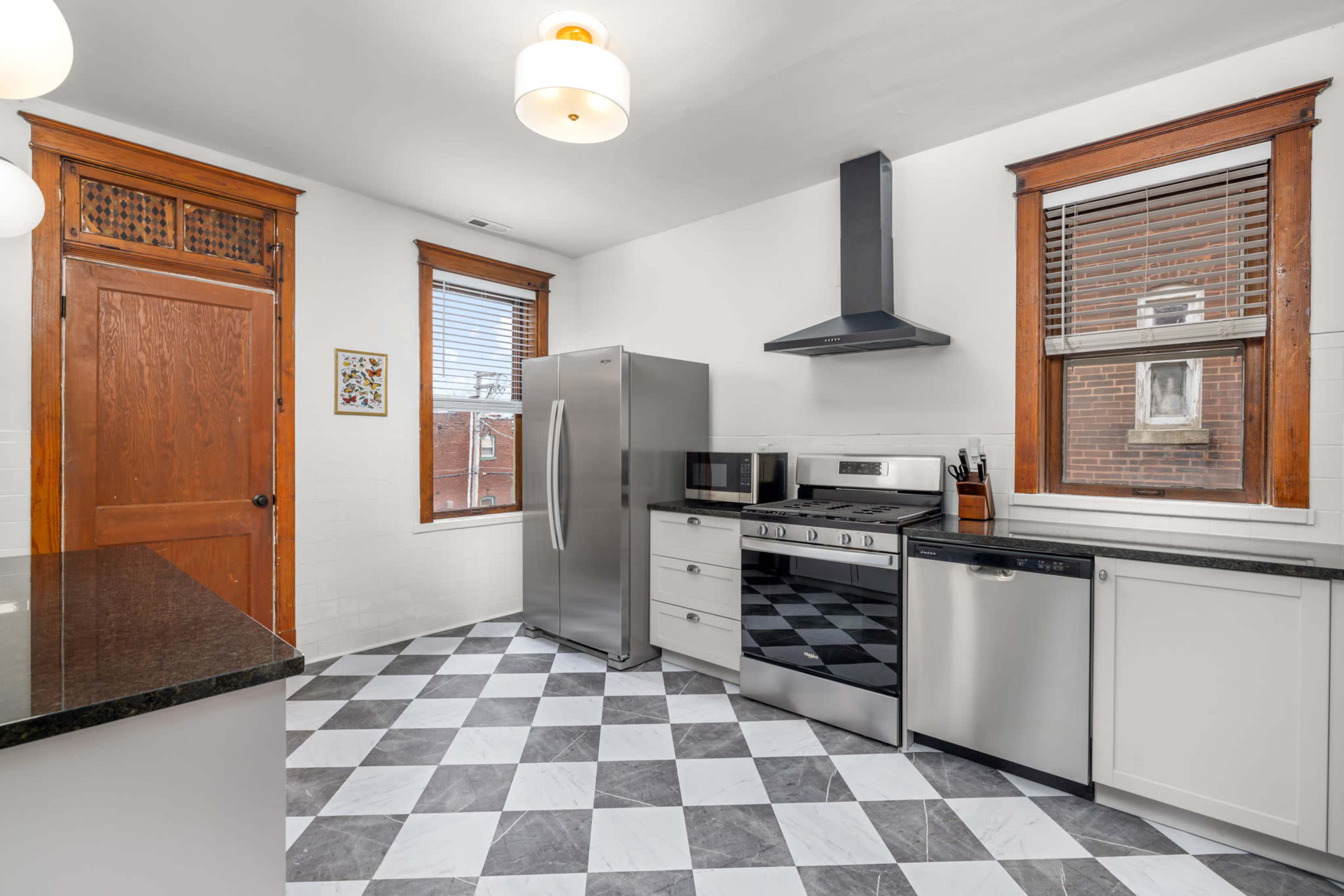 The image shows a modern kitchen with stainless steel appliances, black and white checkered flooring, and wooden cabinets.