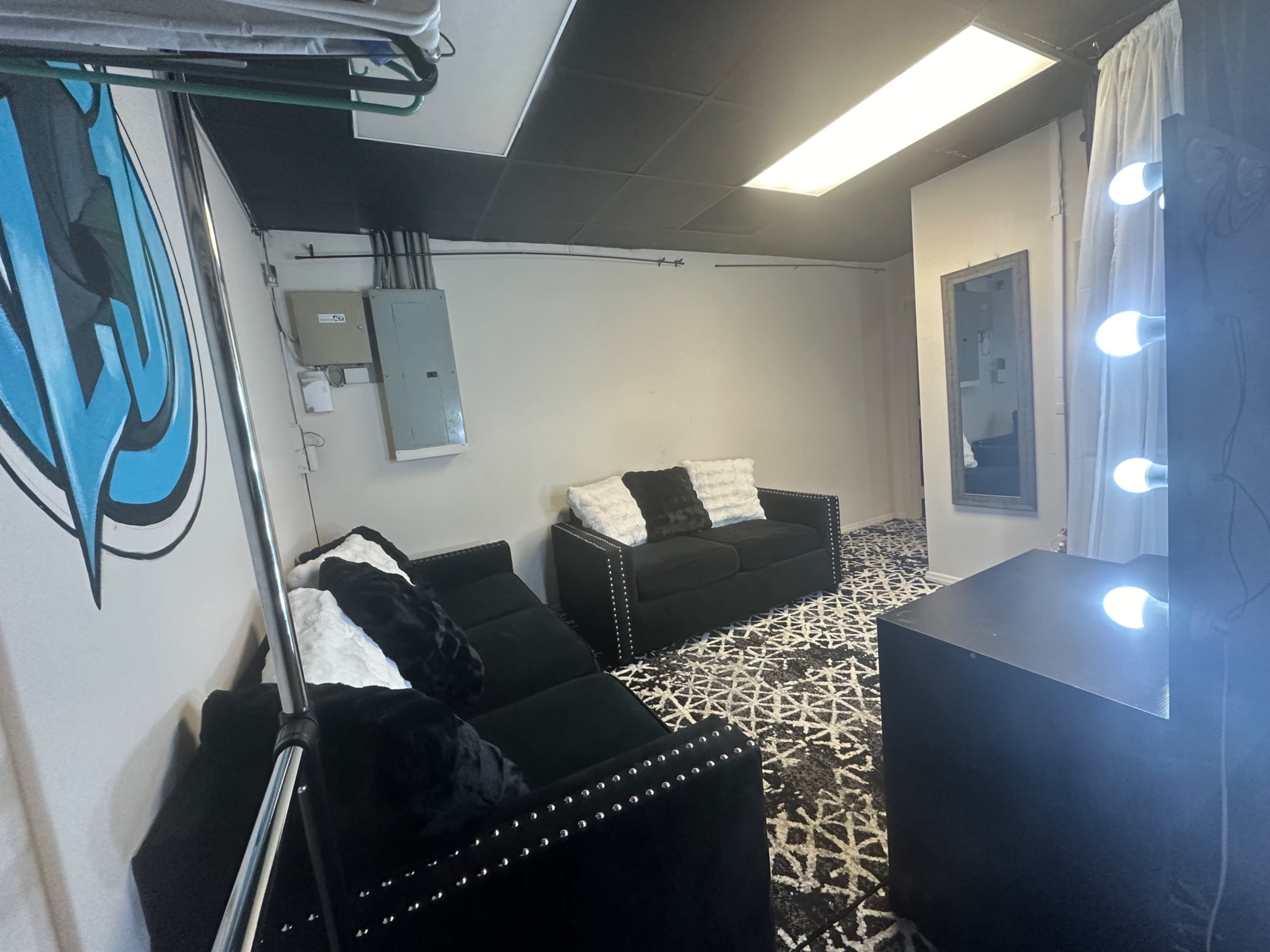 A room with two black sofas, a lighted vanity mirror, and a patterned black and white rug.