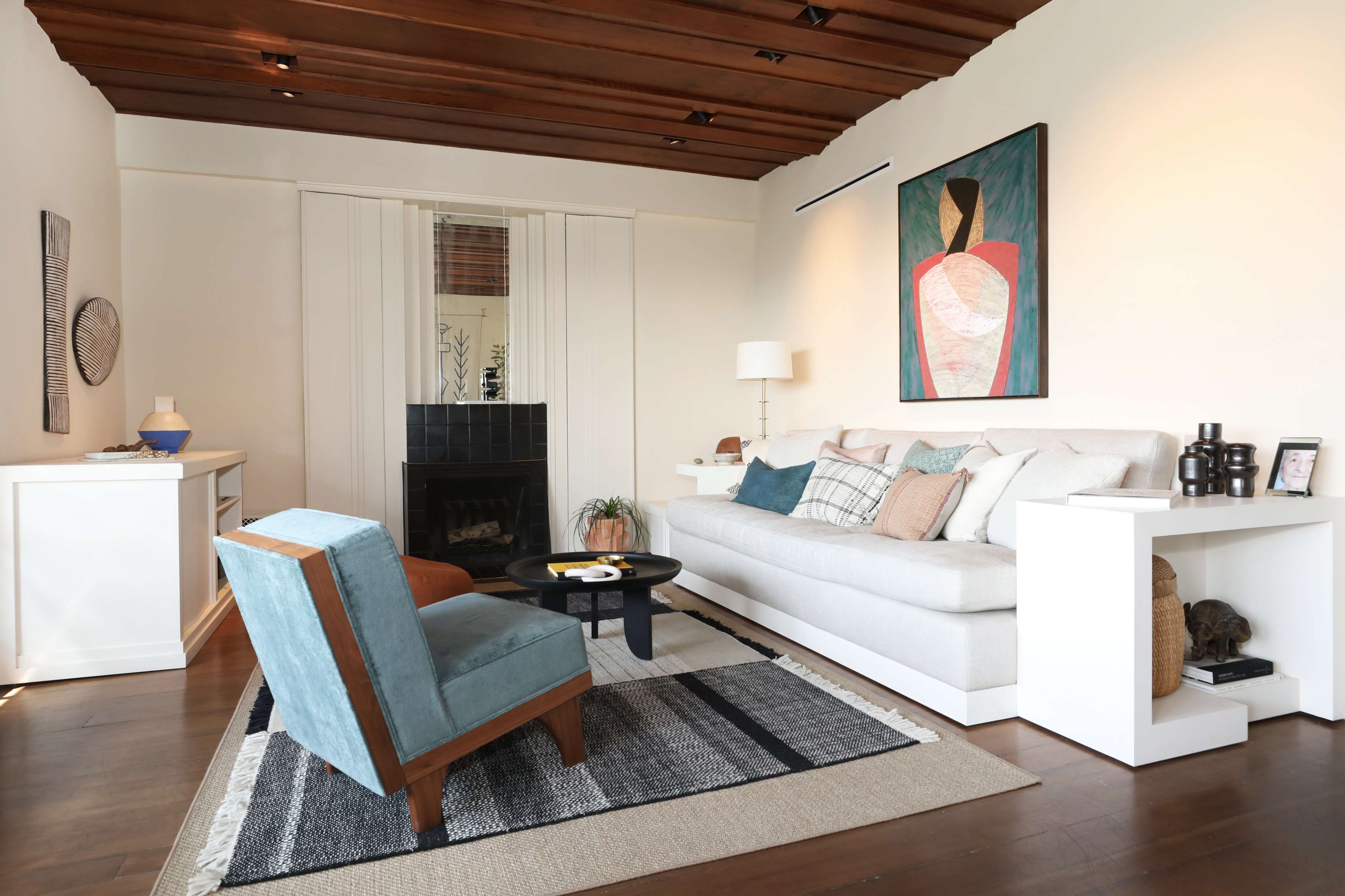 A modern living room with a light-colored sofa, a blue accent chair, a round black coffee table, and a large abstract painting on the wall.