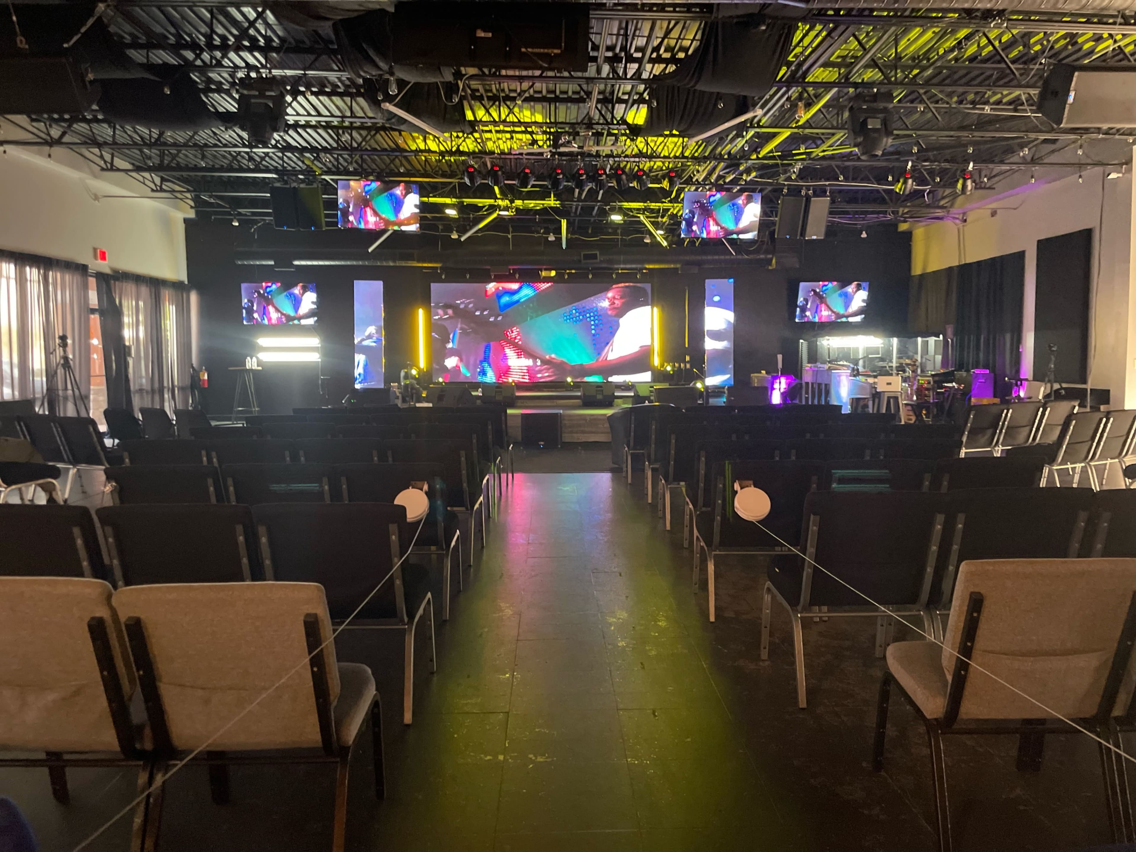 An empty event space with rows of chairs facing a stage and multiple screens displaying vibrant graphics.