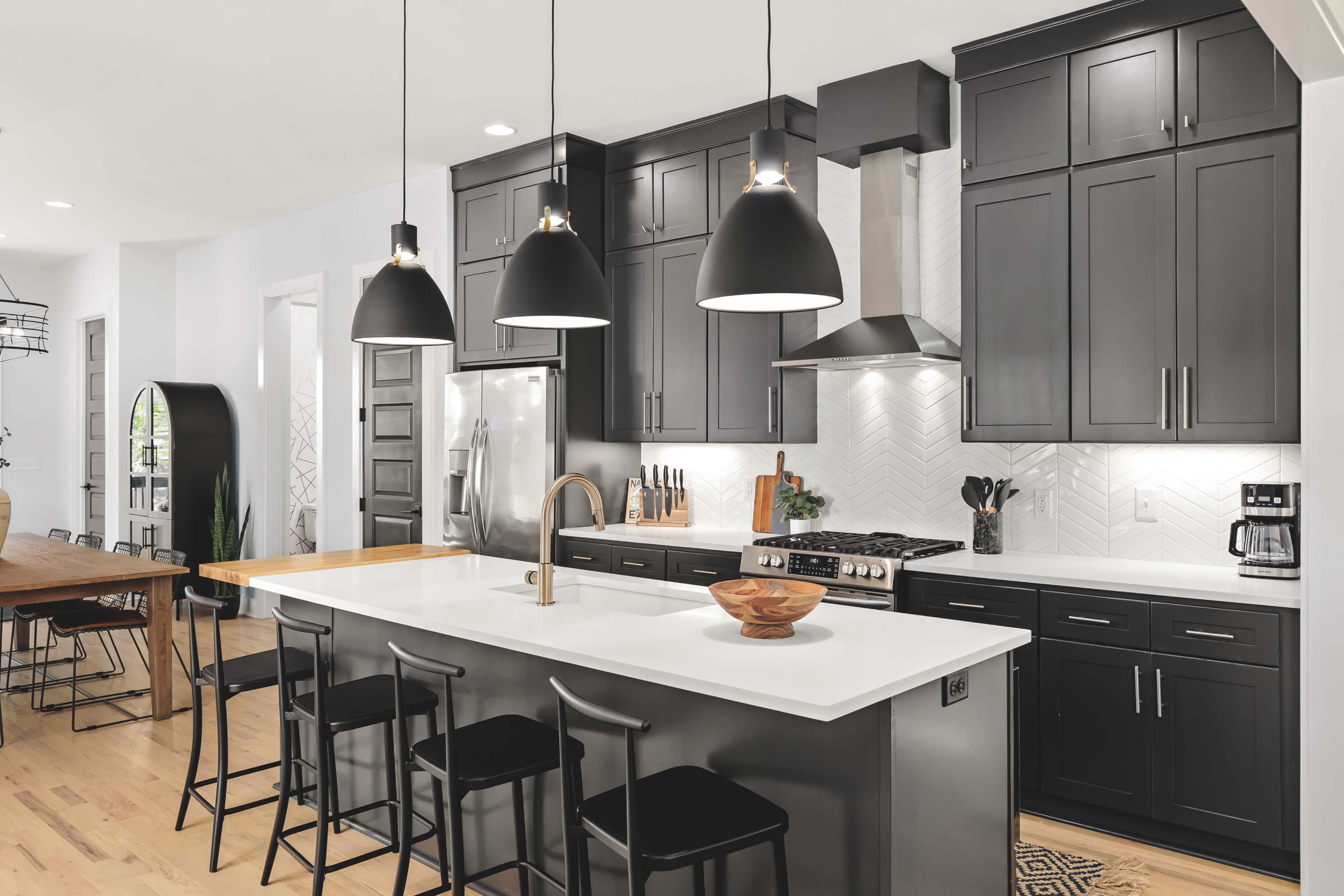 A modern kitchen features black cabinetry, a large island with seating, and pendant lighting over a white countertop.