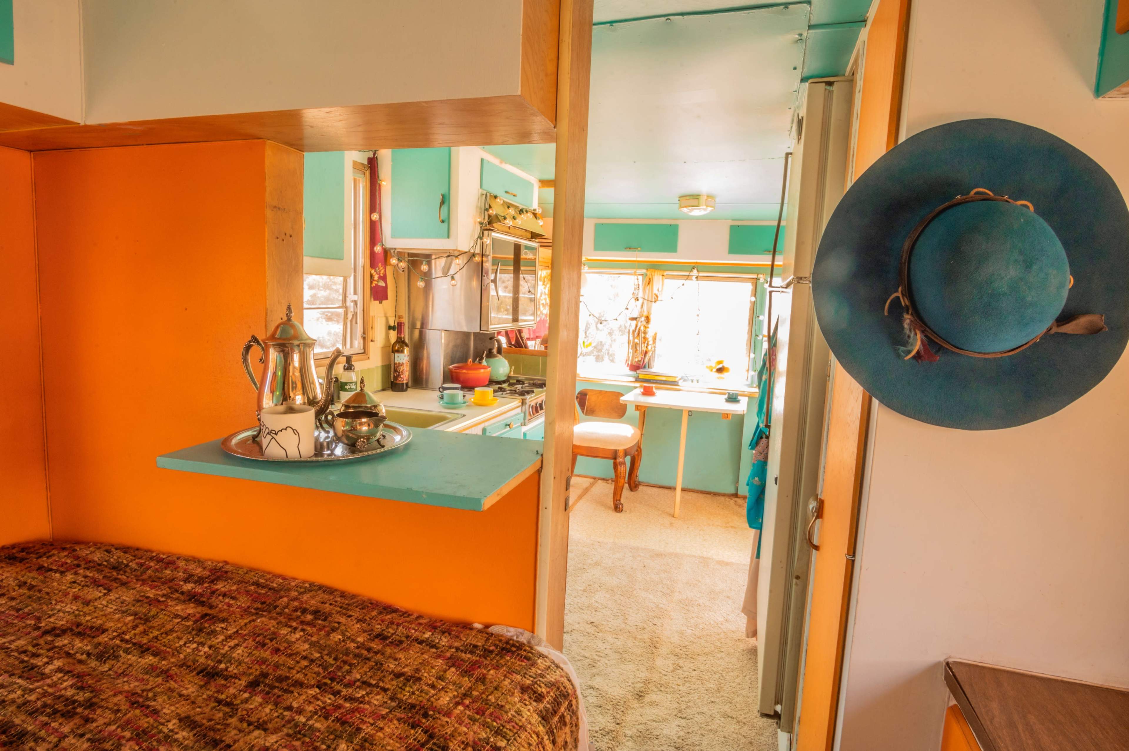 A view of a colorful interior space featuring a kitchen and a bedroom with a teapot on a tray and a hat hanging on the wall.