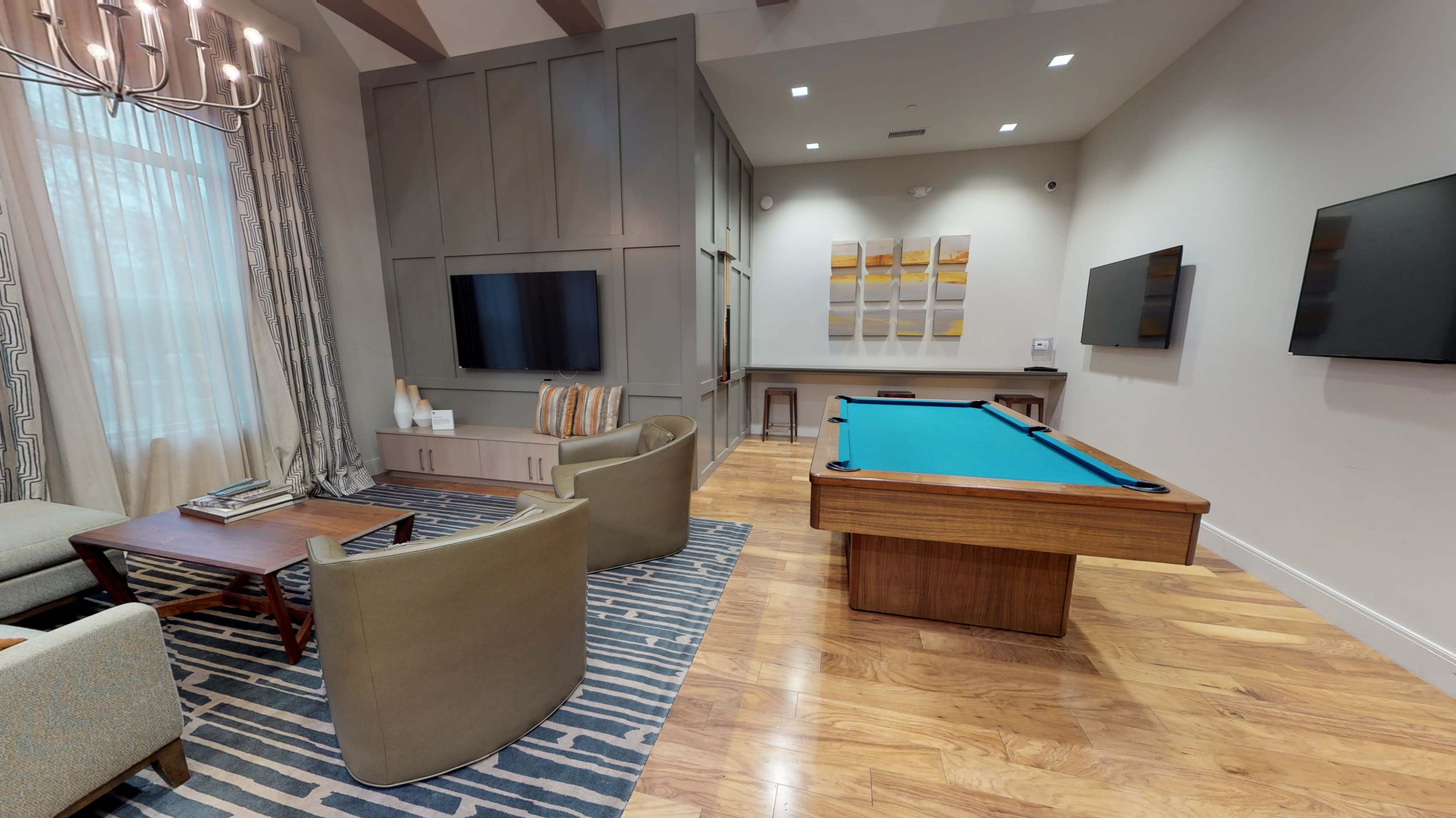 A modern living space featuring a billiards table, two armchairs, a wooden coffee table, and multiple wall-mounted televisions.