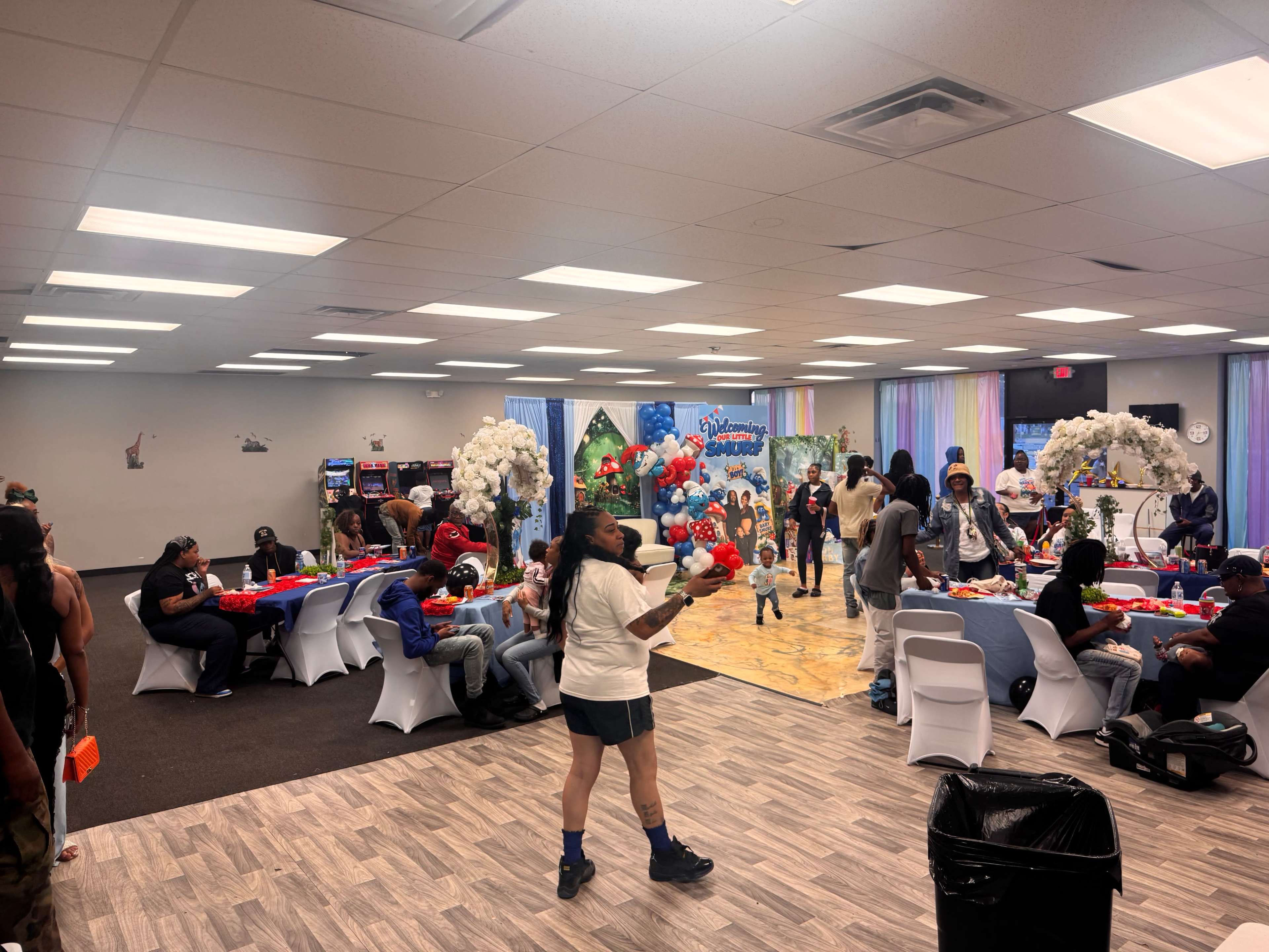 A large indoor event space is decorated with colorful balloons and tables while people socialize and celebrate.