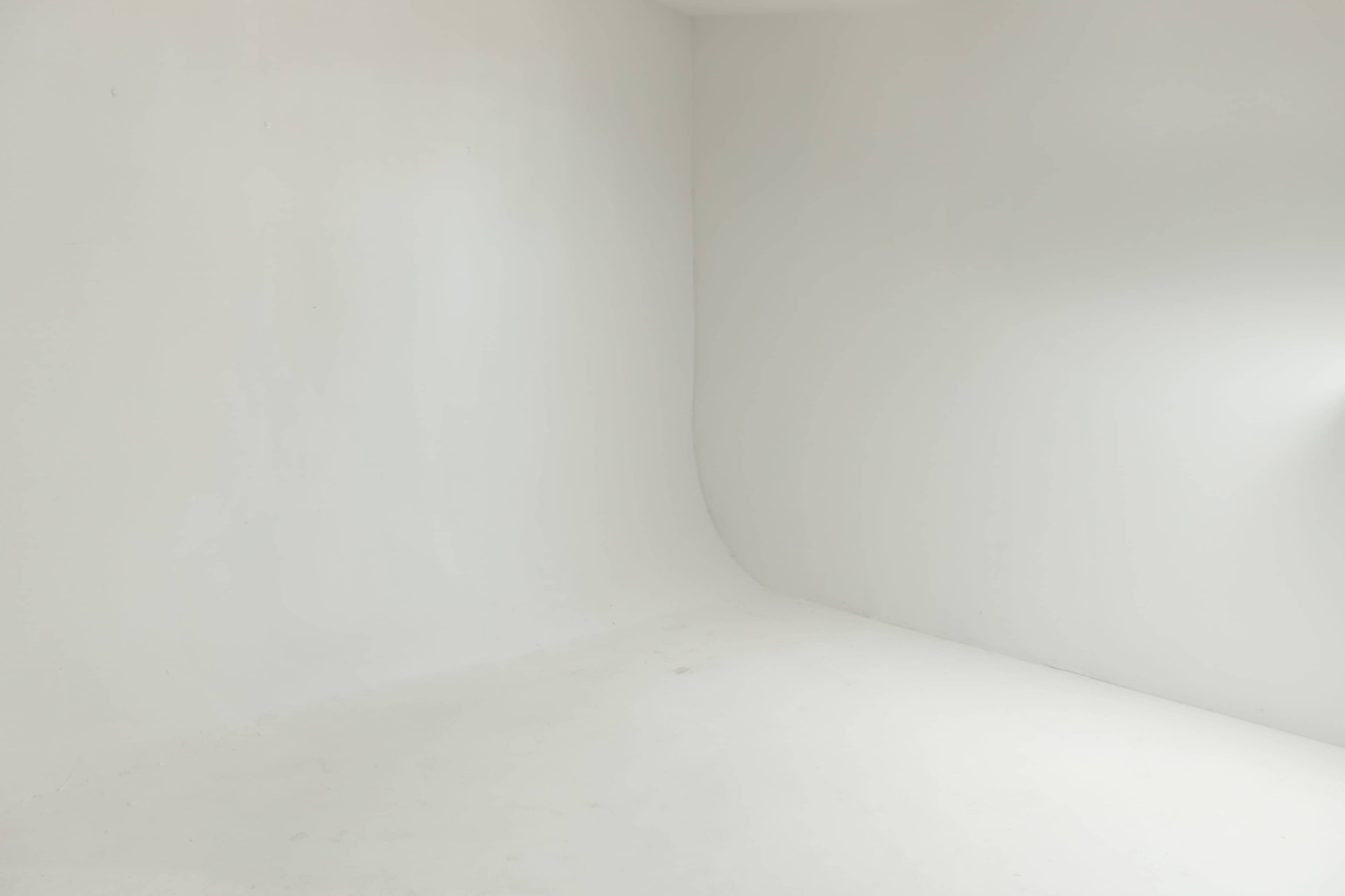 The image shows a blank white room with smooth walls and a curved corner.