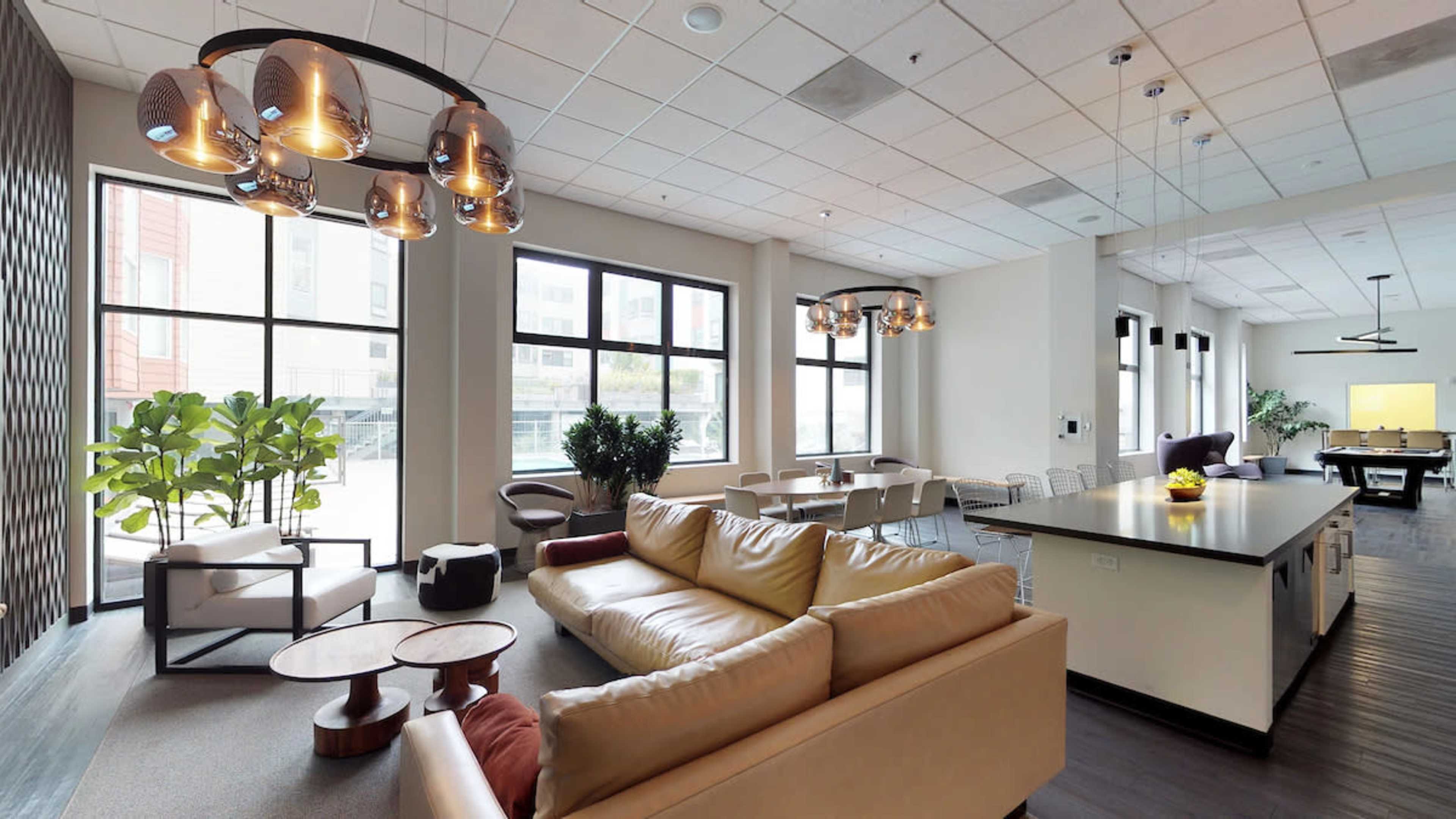 A modern, open-plan lounge area features a leather sofa, a dining table, and large windows allowing natural light to fill the space.