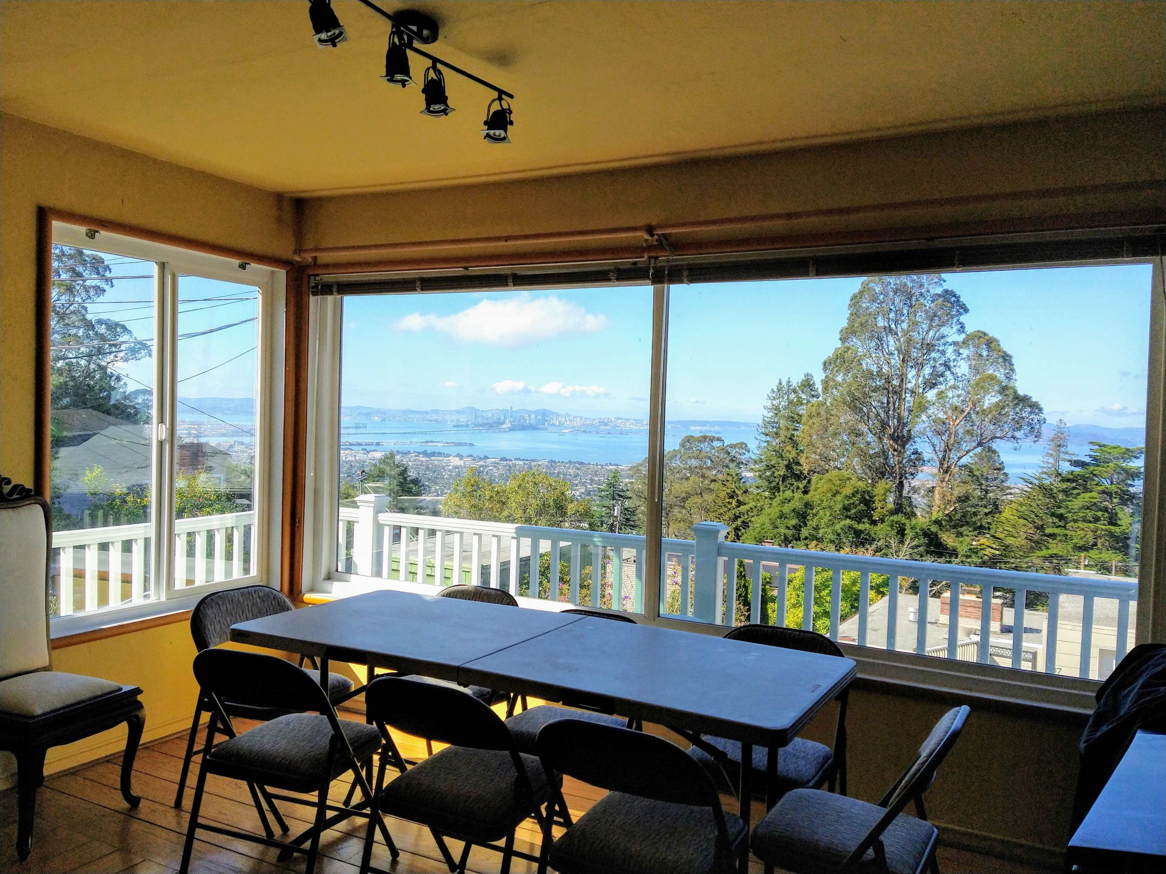 A spacious room with a table and chairs overlooks a scenic view of a bay and distant mountains through large windows.