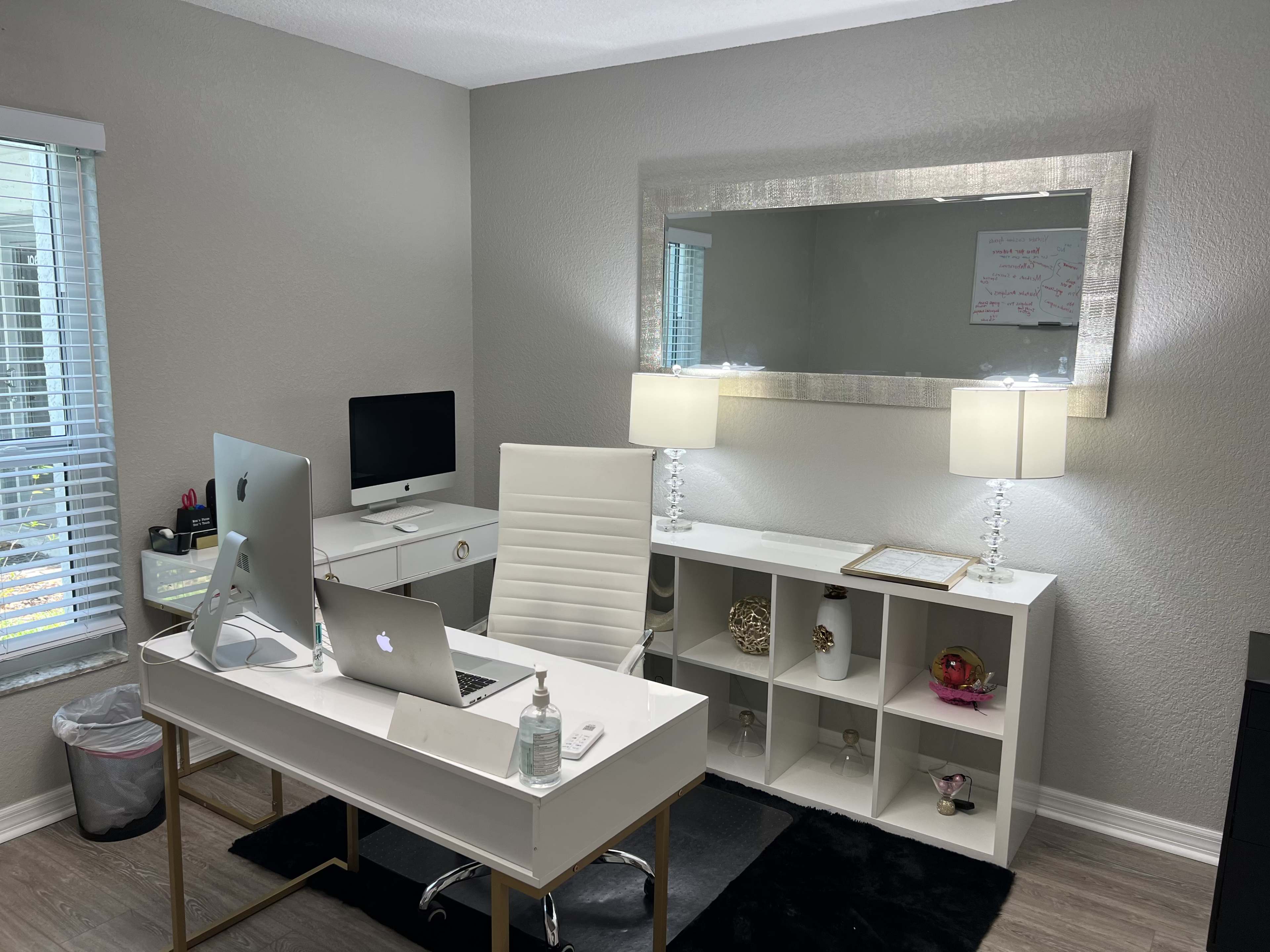 A modern home office with a white desk, computer setup, two table lamps, and storage cubicles against a gray wall.