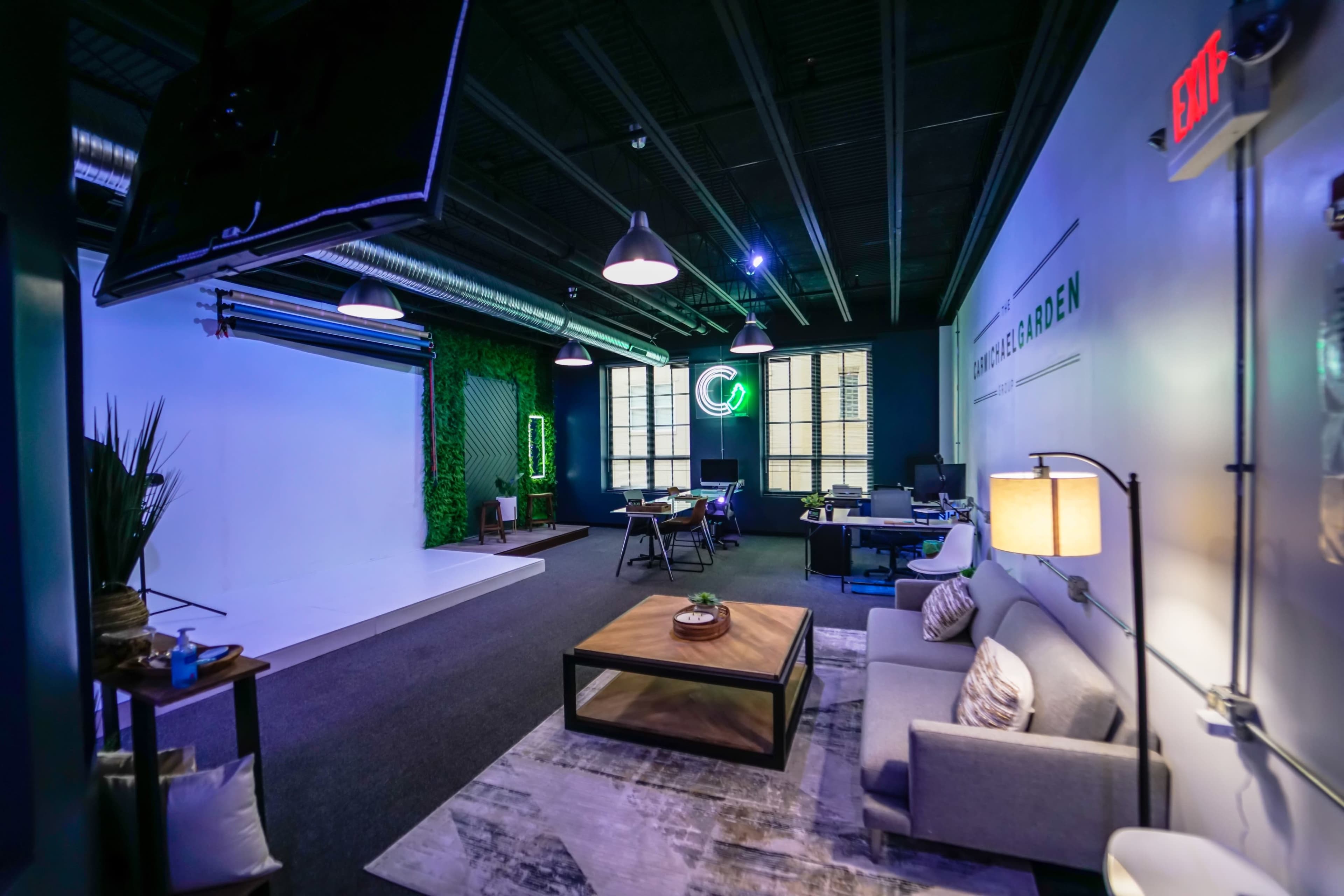 A modern studio space with a seating area, a green wall, and equipment for photography and production.