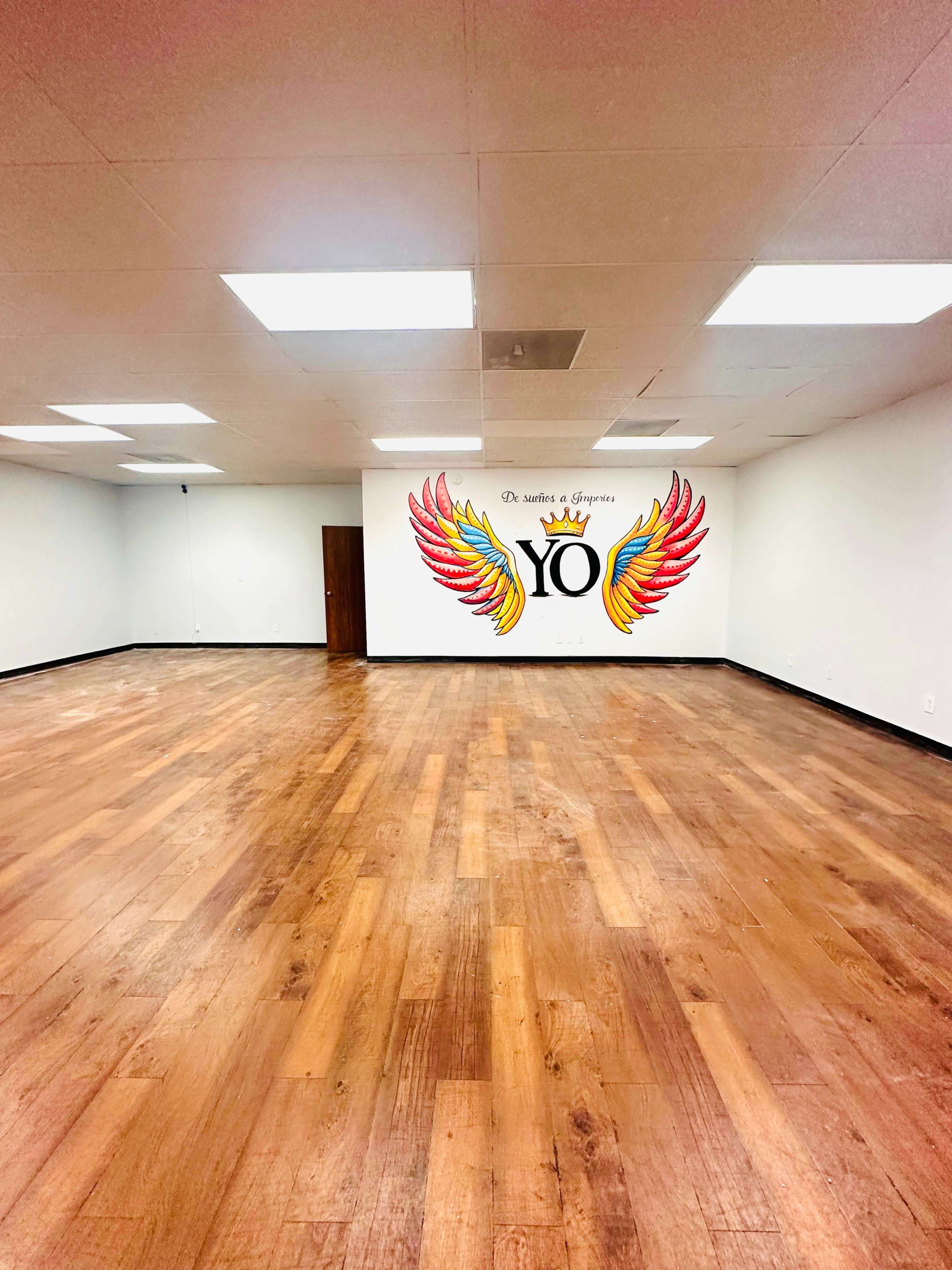 A spacious room with wooden floors, featuring a wall mural of colorful wings and the word "YO."