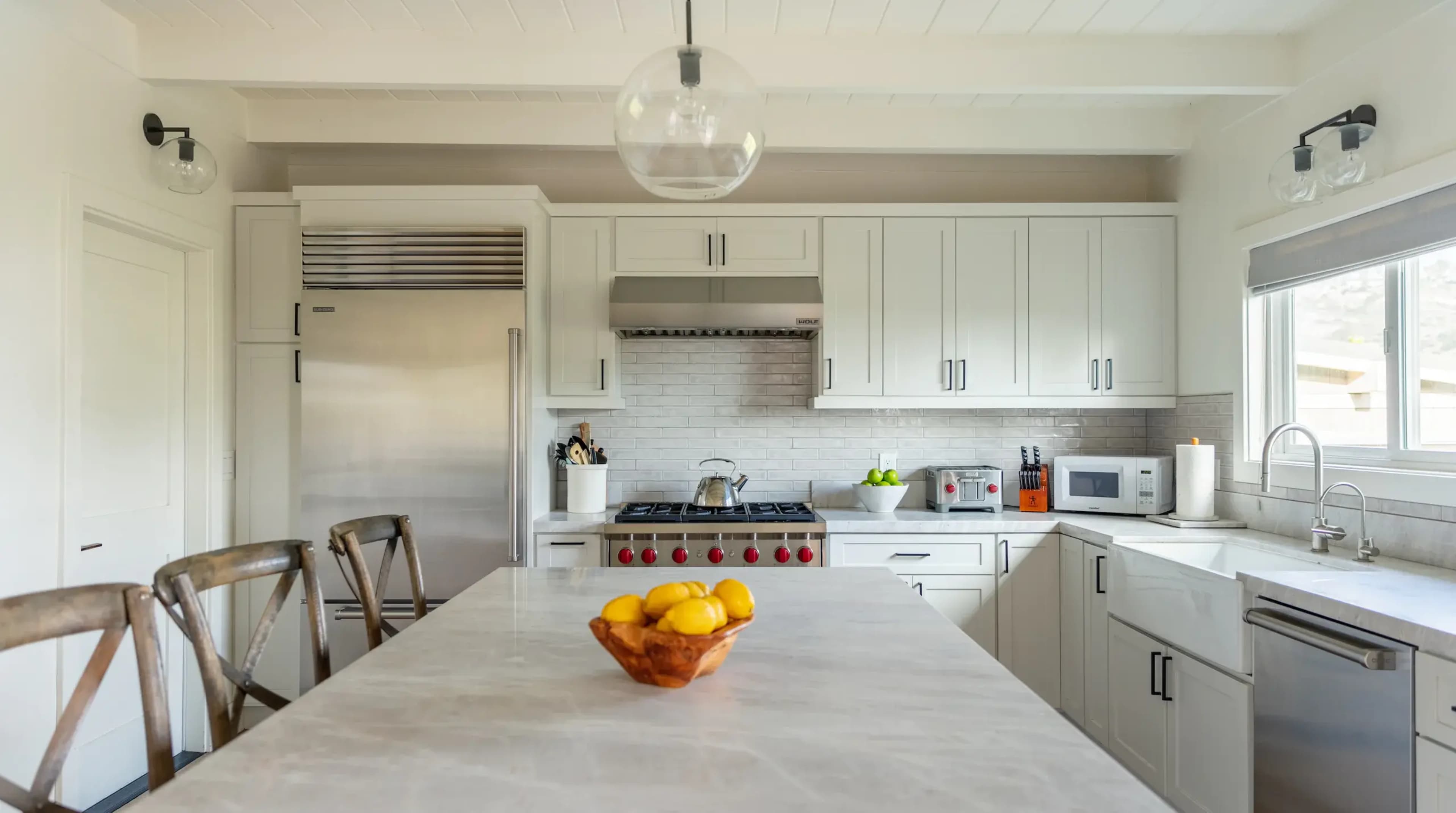 A modern kitchen features white cabinetry, stainless steel appliances, and a central island with a bowl of citrus fruits.