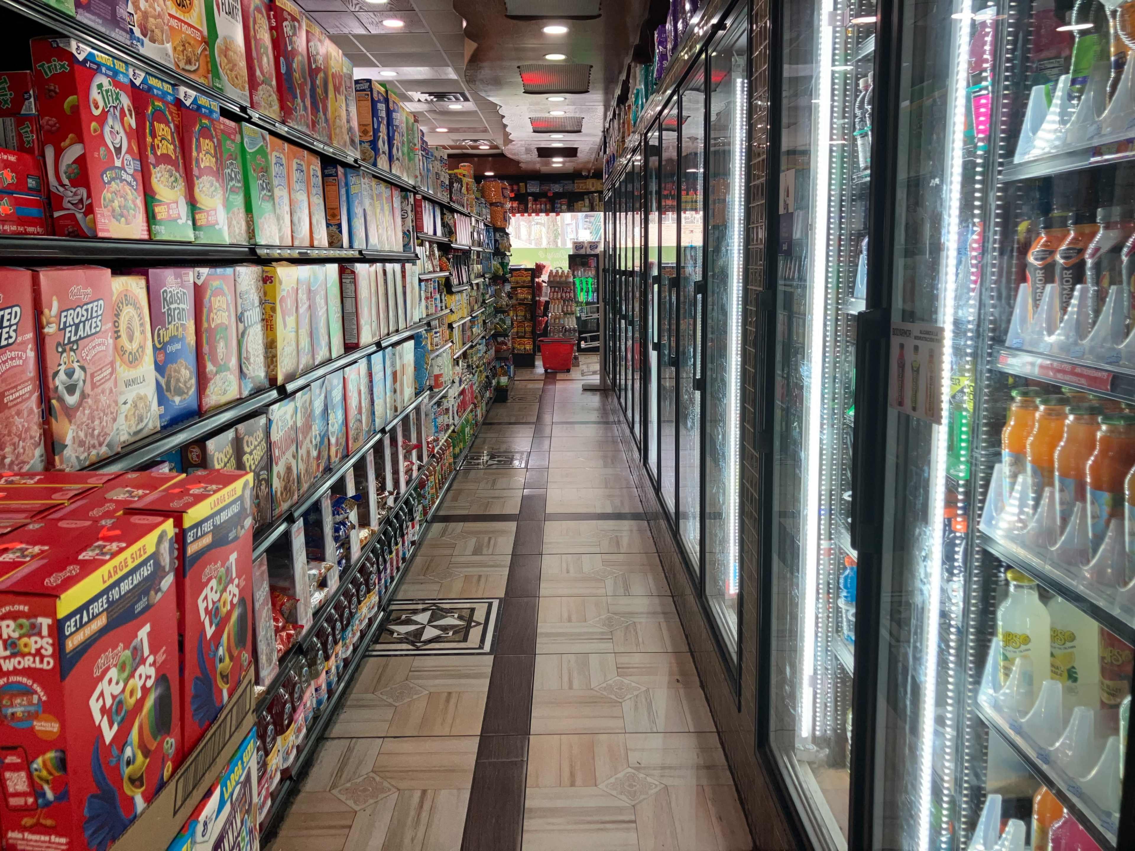 A grocery store aisle lined with shelves of cereal boxes on one side and refrigerated display cases on the other.