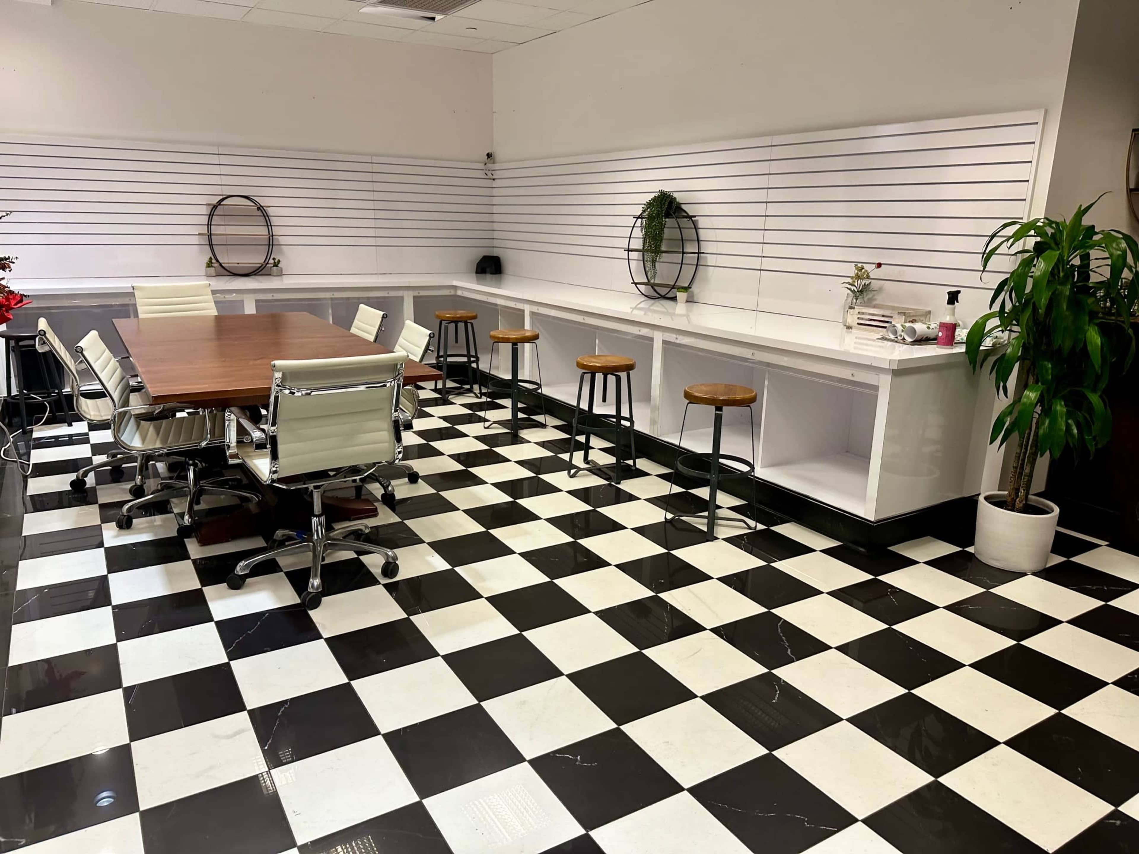 The room features a large wooden table surrounded by white chairs, with bar stools along a counter, all set on a black and white checkered floor.