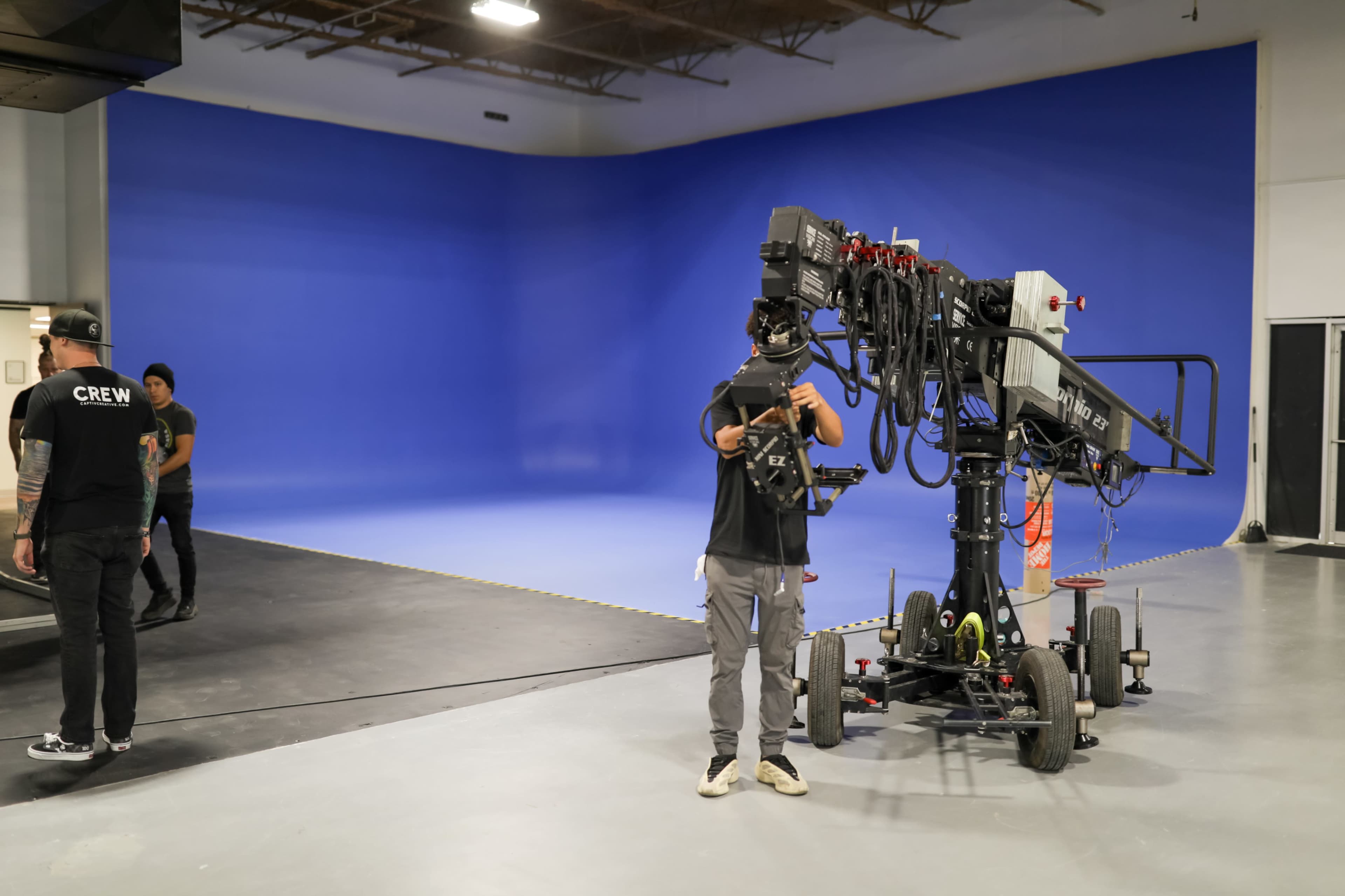 A film crew sets up equipment in a studio with a blue backdrop.