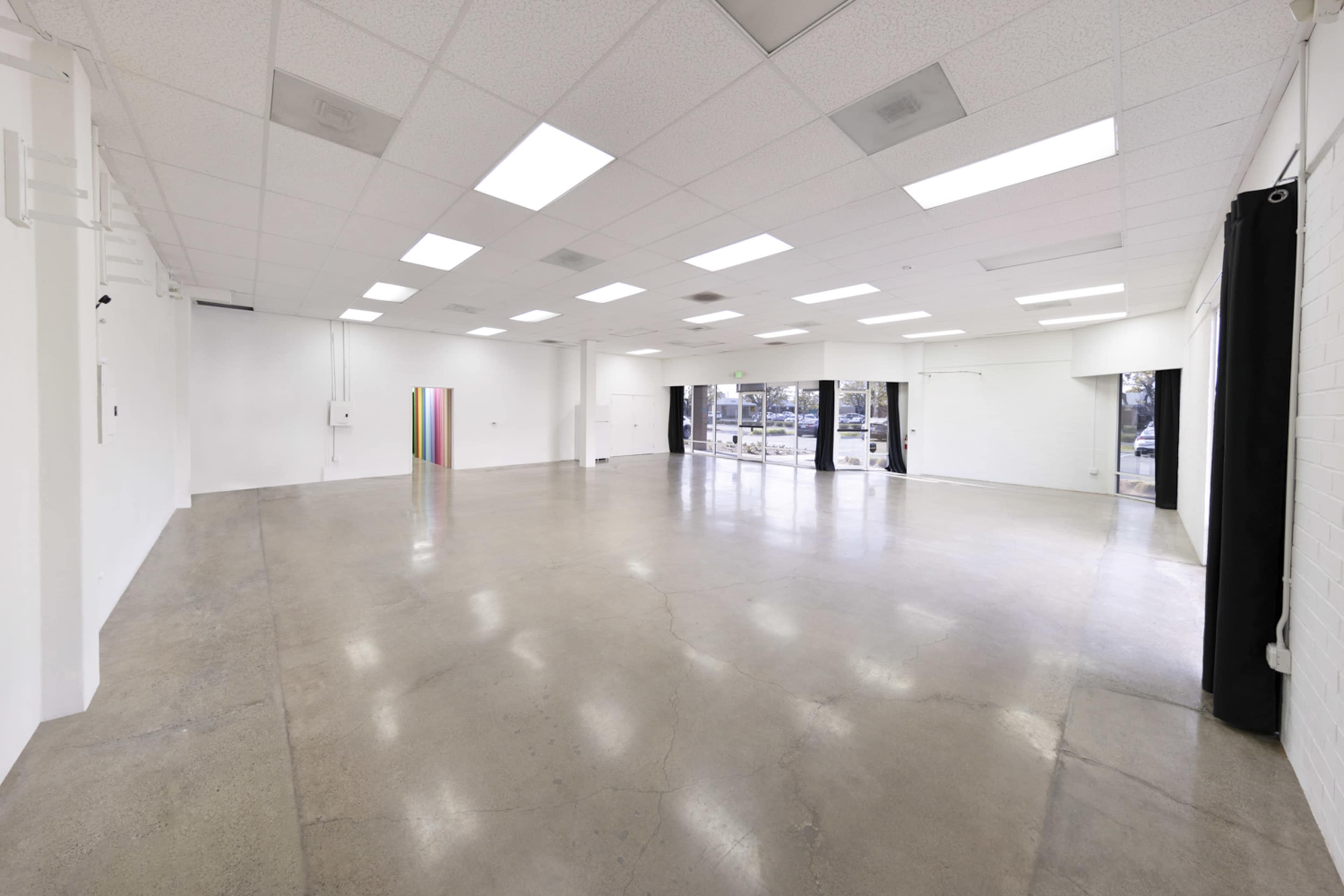 A spacious, empty interior room with concrete flooring and large windows facing the street.